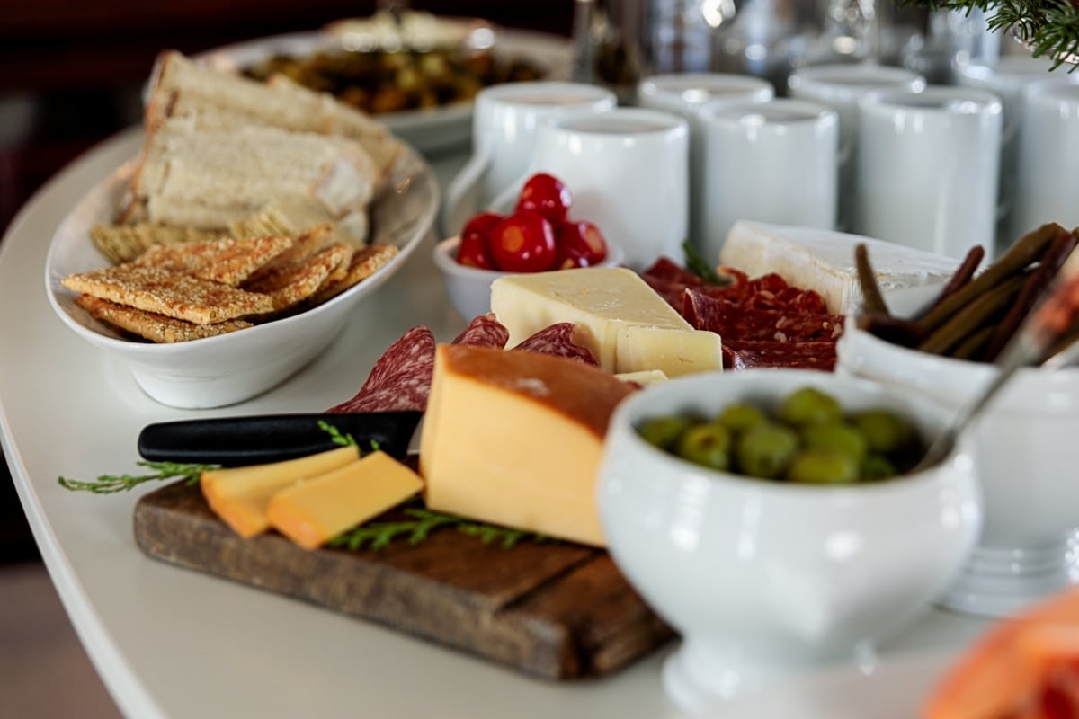 White table filled with a spread of holiday side dishes including olives, crackers, cheese, meat, peppers, and more.