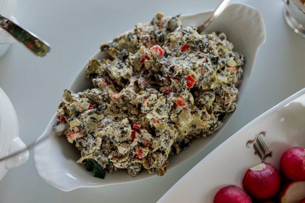 White oval bowl filled with spinach dip sitting on white table with radishes to the side.