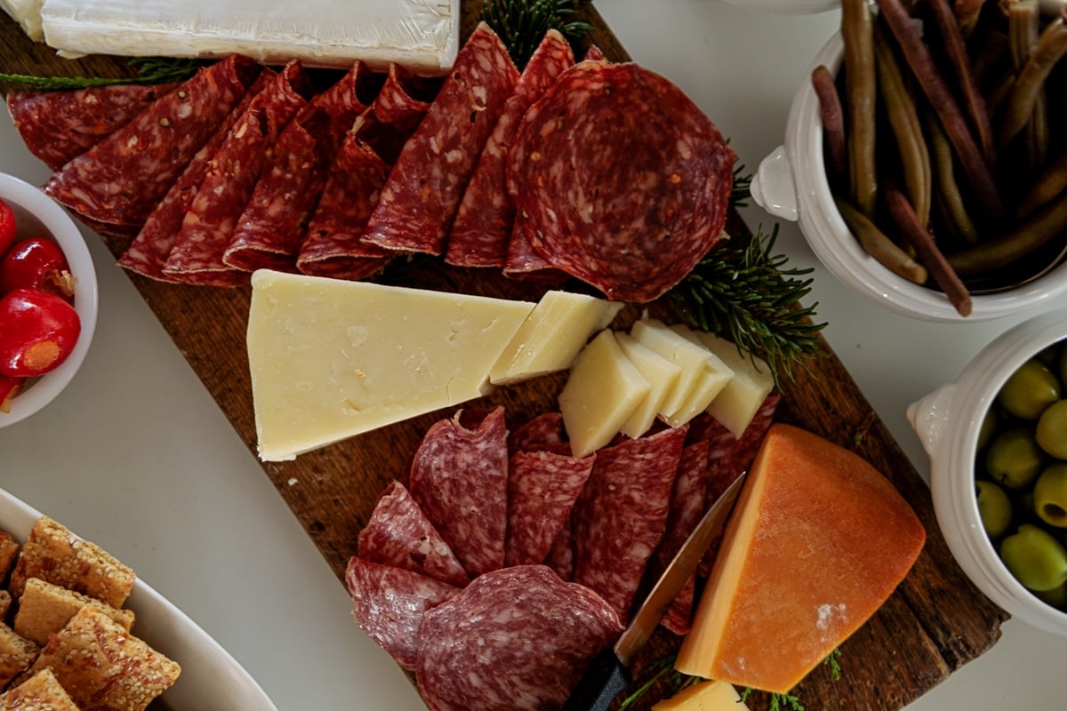 Charcuterie board filled with blocks of cheese and meats sitting on white table for a holiday party.