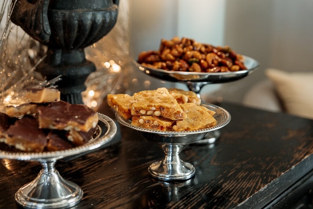 Black side table with three silver containers filled with Christmas candy and nuts.