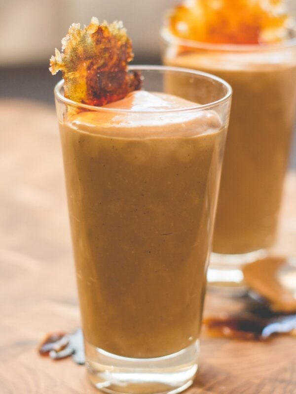 Tall glass filled with butterscotch pudding with browned piece of sugar on top all on wood cutting board surface