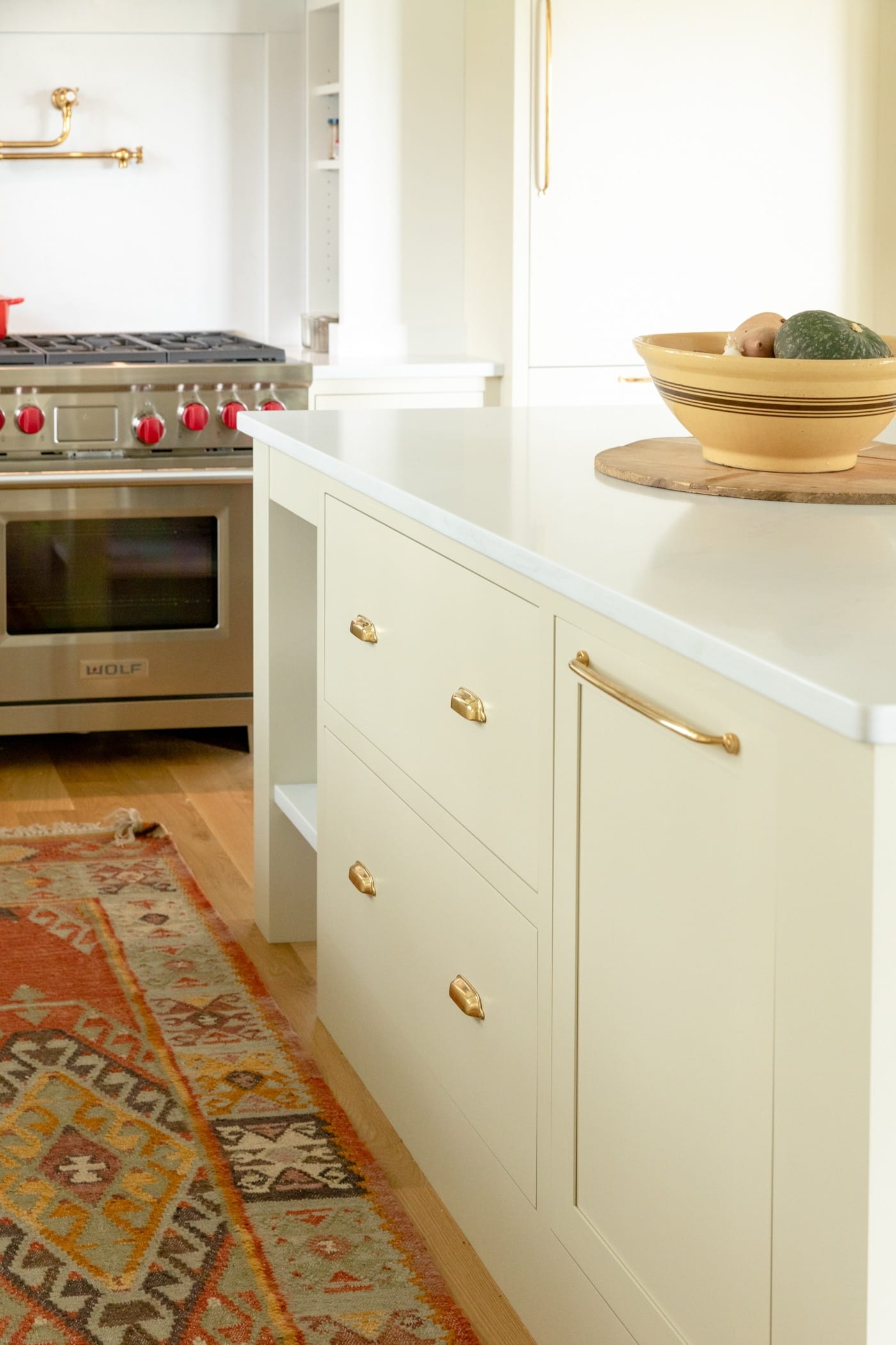 Large drawers in a kitchen island with range in background and red rug on hardwood floors