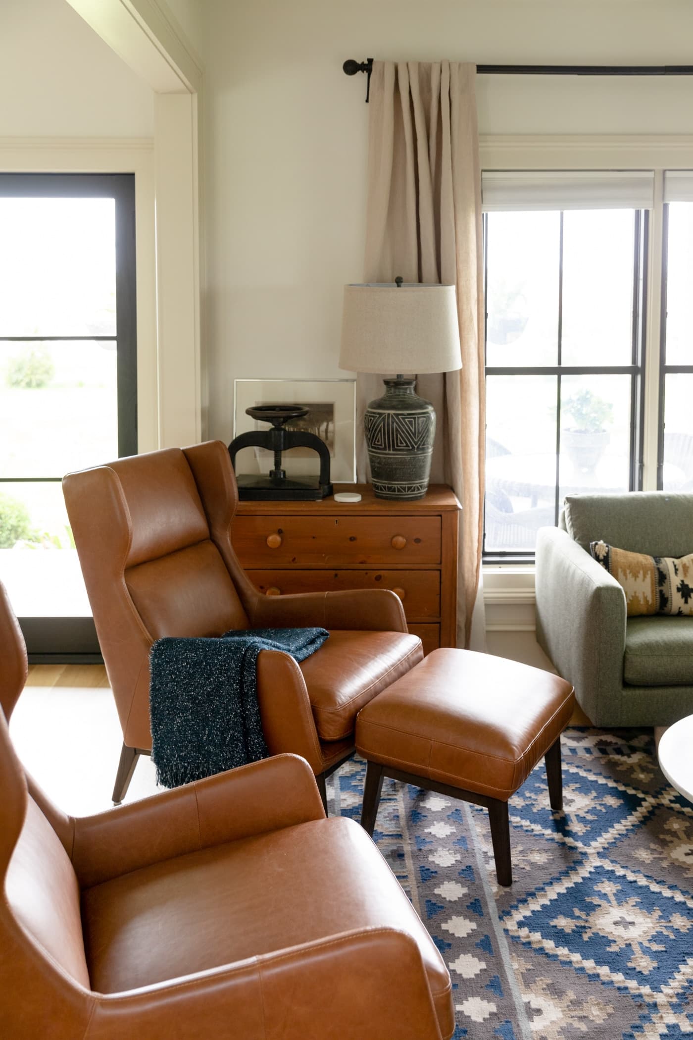 Two brown leather chairs sitting on blue colored rug with pine chest and black French door in background