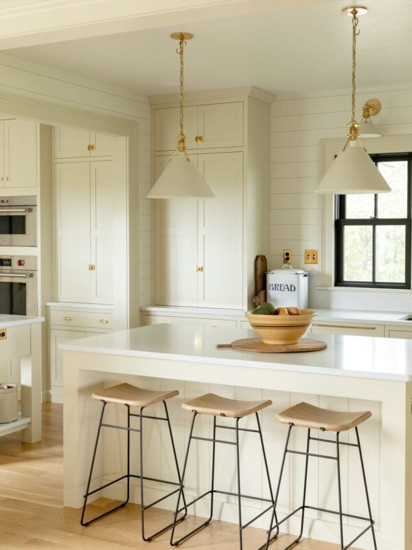 Kitchen stools sitting at a large island in a farmhouse kitchen with black windows and pantry cabinet in background