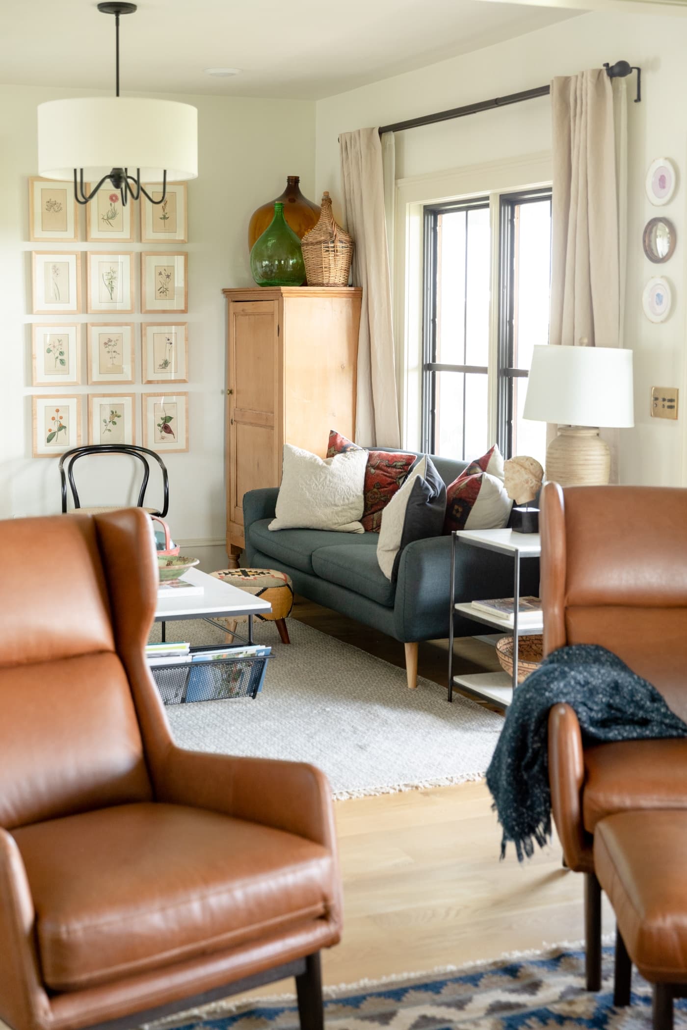 Two leather chairs with blue couch with red pillows in background all with white walls and light oak flooring