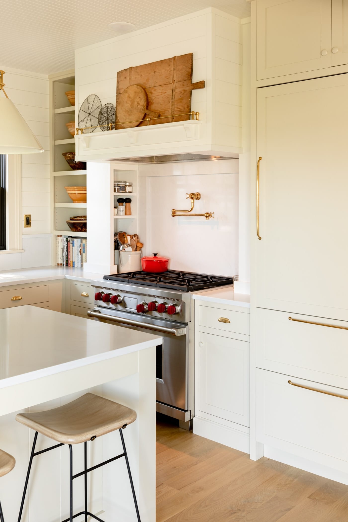Large stainless steel range with red knobs surrounded by cabinetry and vent above with cutting boards sitting on a wooden shelf