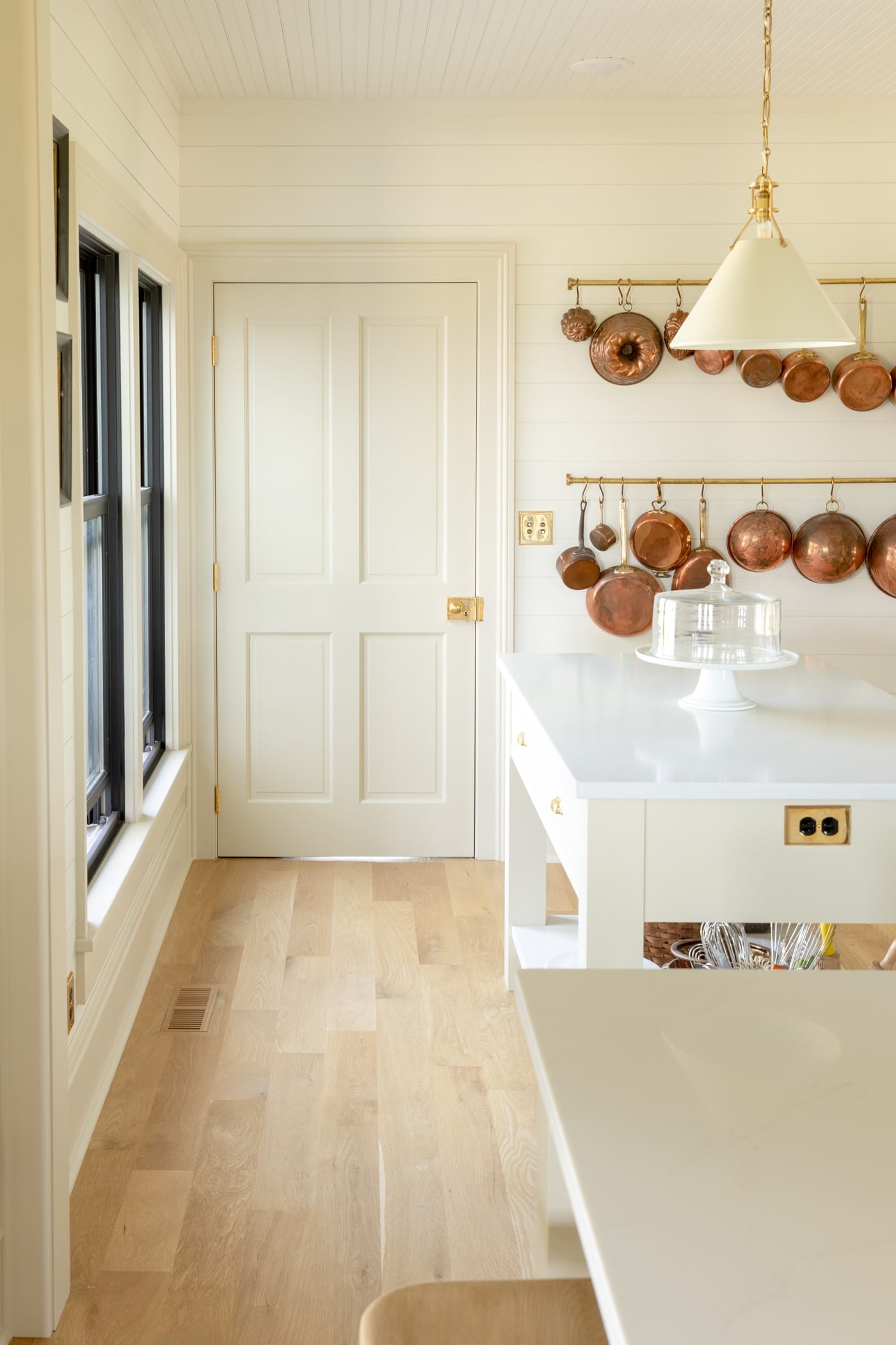 Four square creamy colored panel door with light oak floors leading up to it with small island to the side