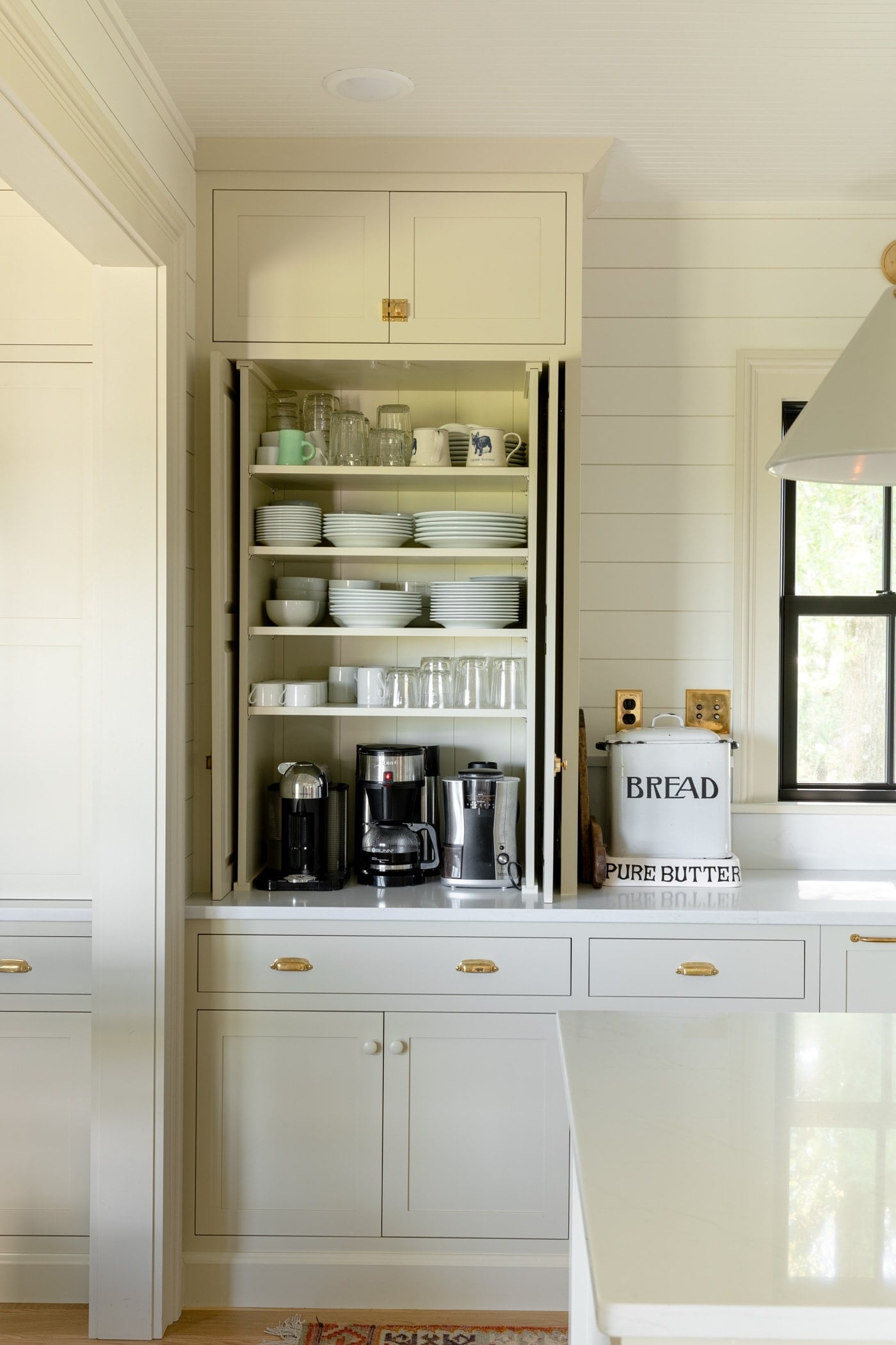 Large upper cabinet sitting on countertop with doors open revealing plates, mugs, bowls, and coffee maker