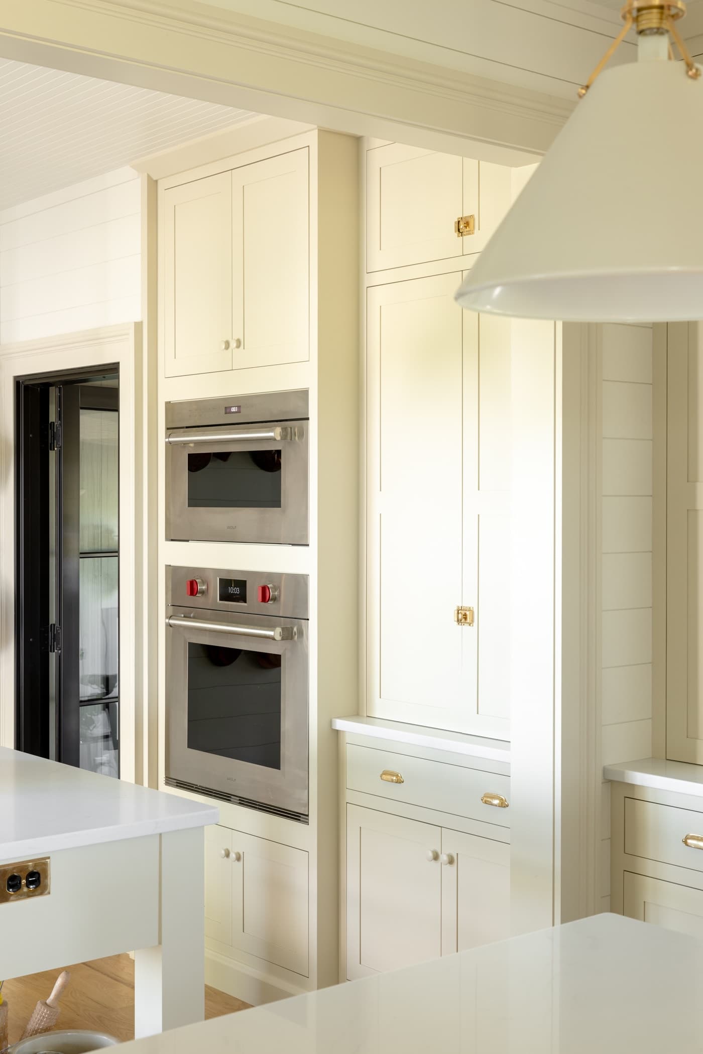 Wall oven in a creamy white cabinet with pantry cabinet right beside it with black door in distance