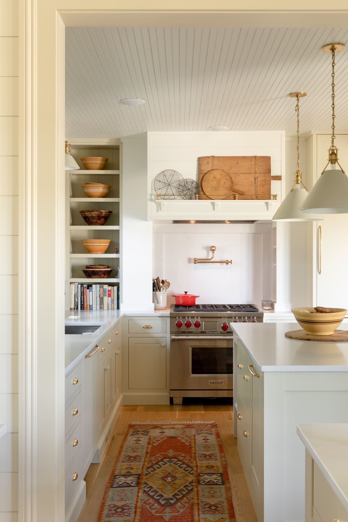 Stainless steel oven with red knobs at far end of kitchen with red rug on wood floors with side of island exposed