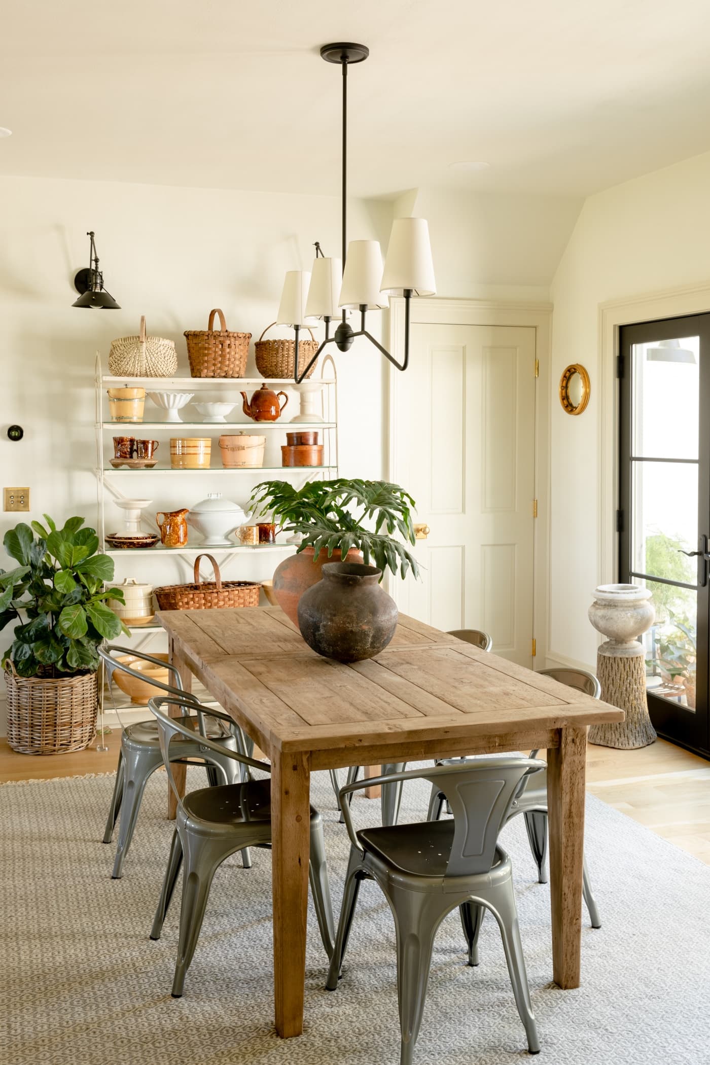 Light wood dining table with steel chairs and large white shelf stacked with brown and yellow decor with black French door to the side