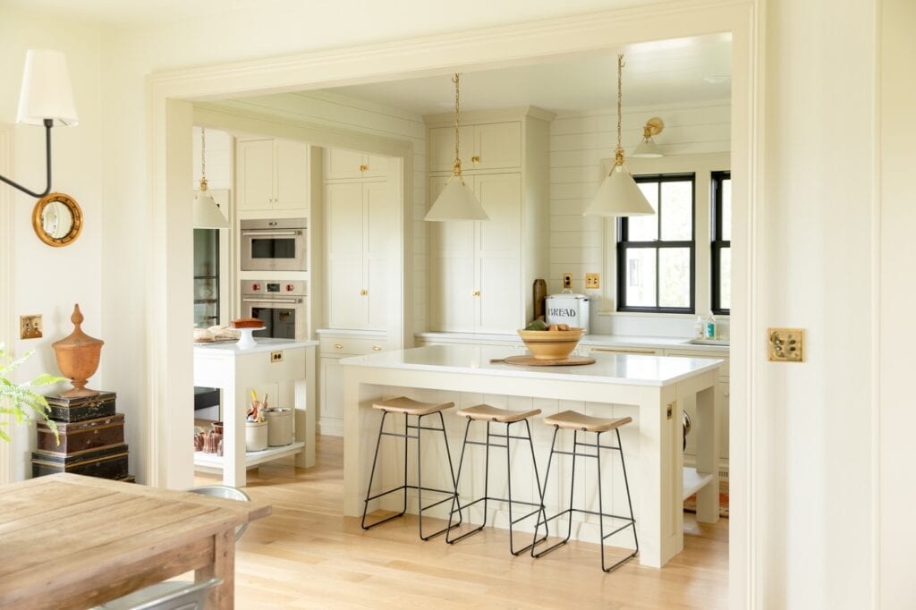 Creamy and light farmhouse kitchen with large island and three stool tucked away with wall oven and black windows