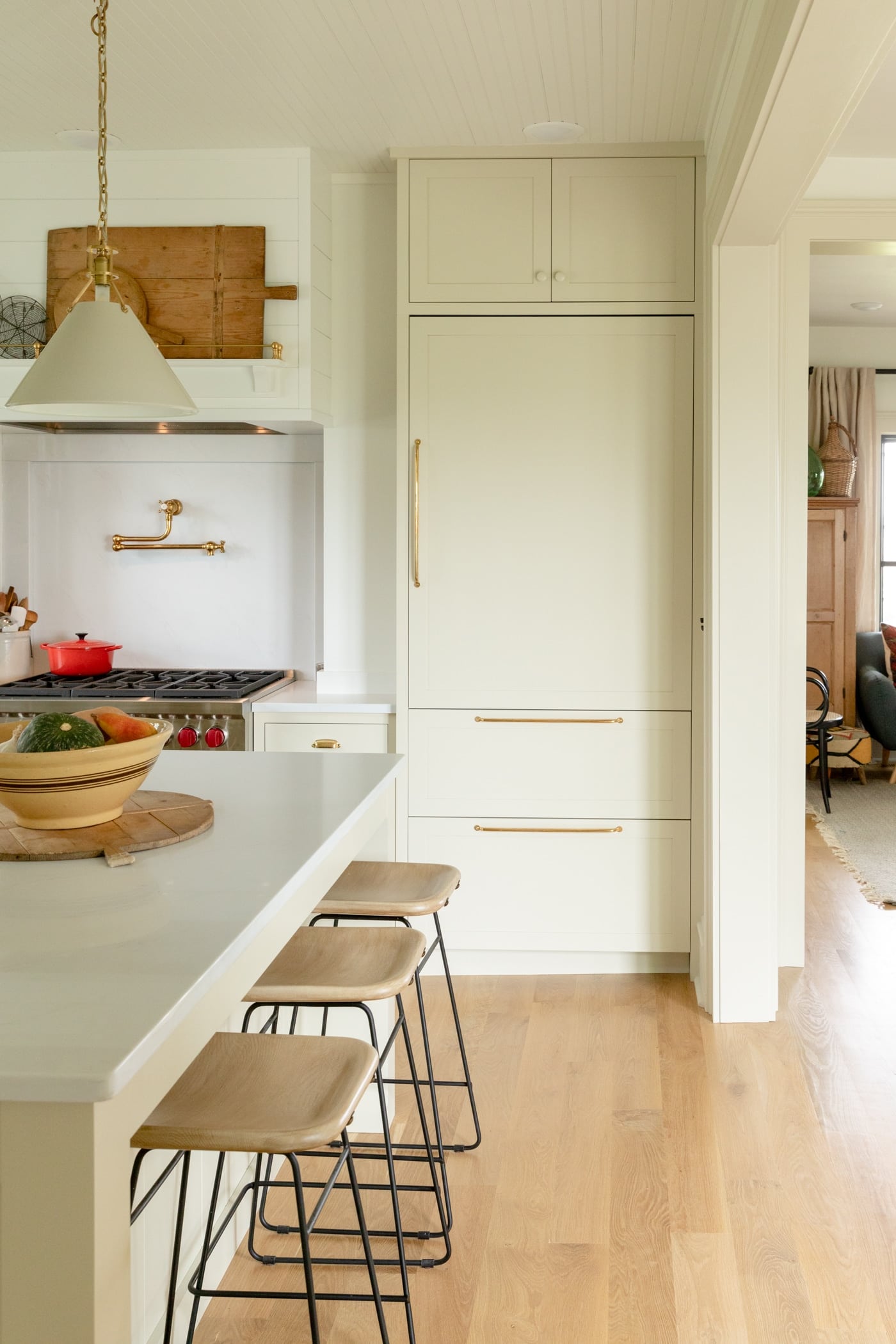 Large panel front refrigerator sitting behind island with stools and light hardwood floors