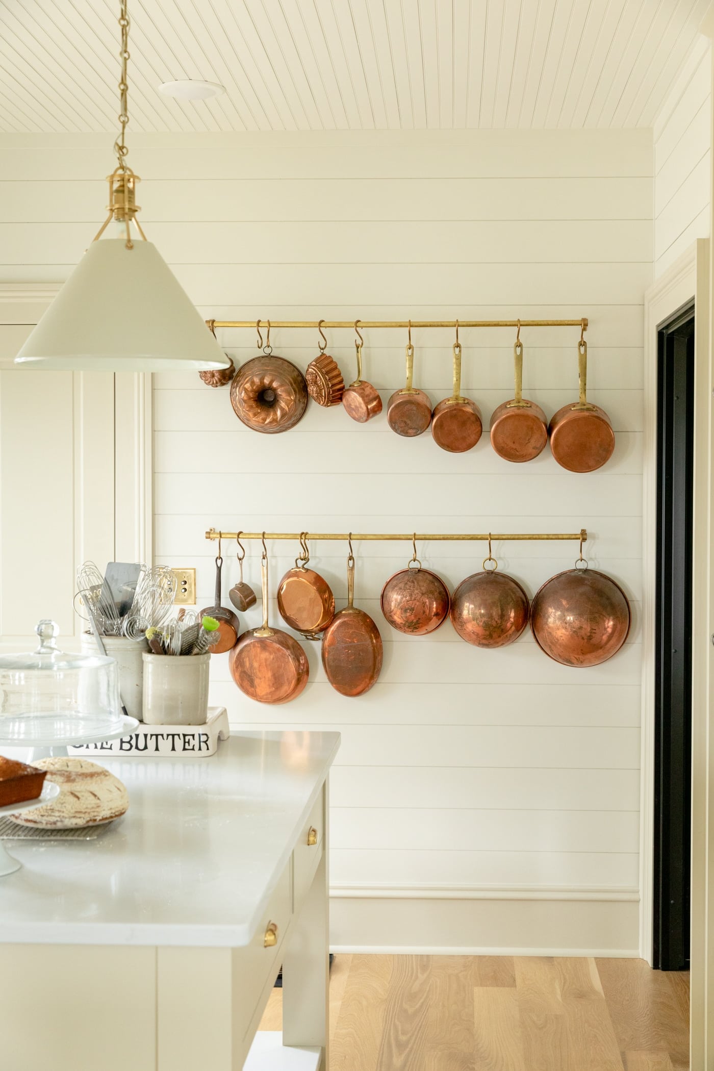 Lots of copper pots hanging on a brass rail with ship lap and large baseboard all with light wood floors