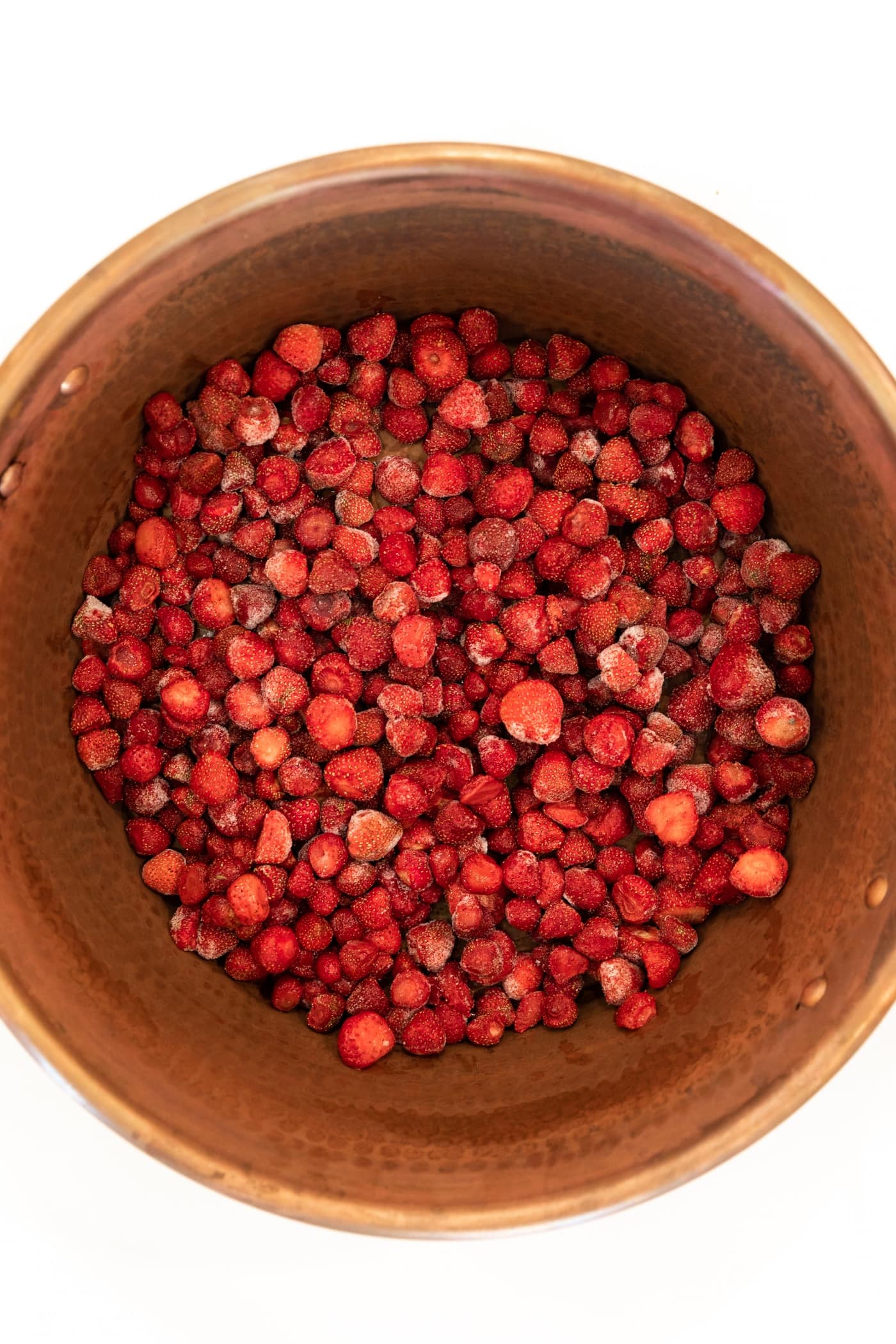 Top down view of frozen strawberries in copper kettle sitting one white countertop