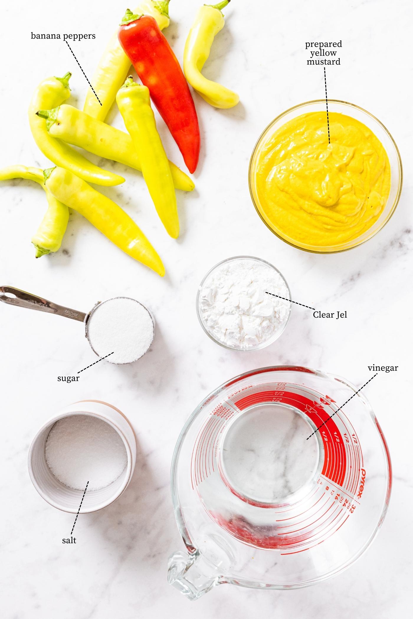 Marble countertop filled with everything needed to make hot pepper mustard including hot peppers, yellow mustard, Clear Jel, vinegar, sugar, and more.