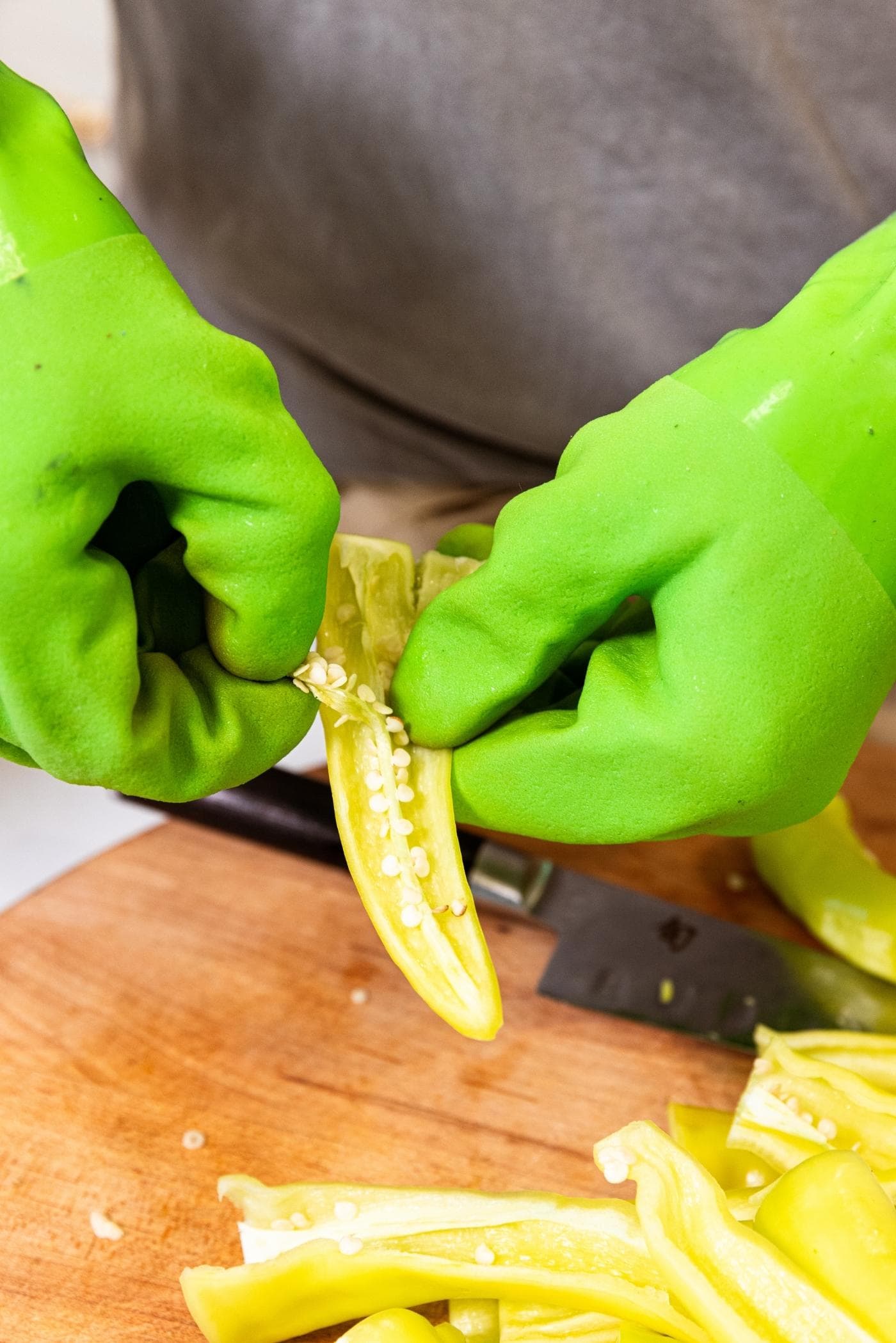 Two hands in green plastic gloves pulling the seeds out of the middle of a hot pepper.