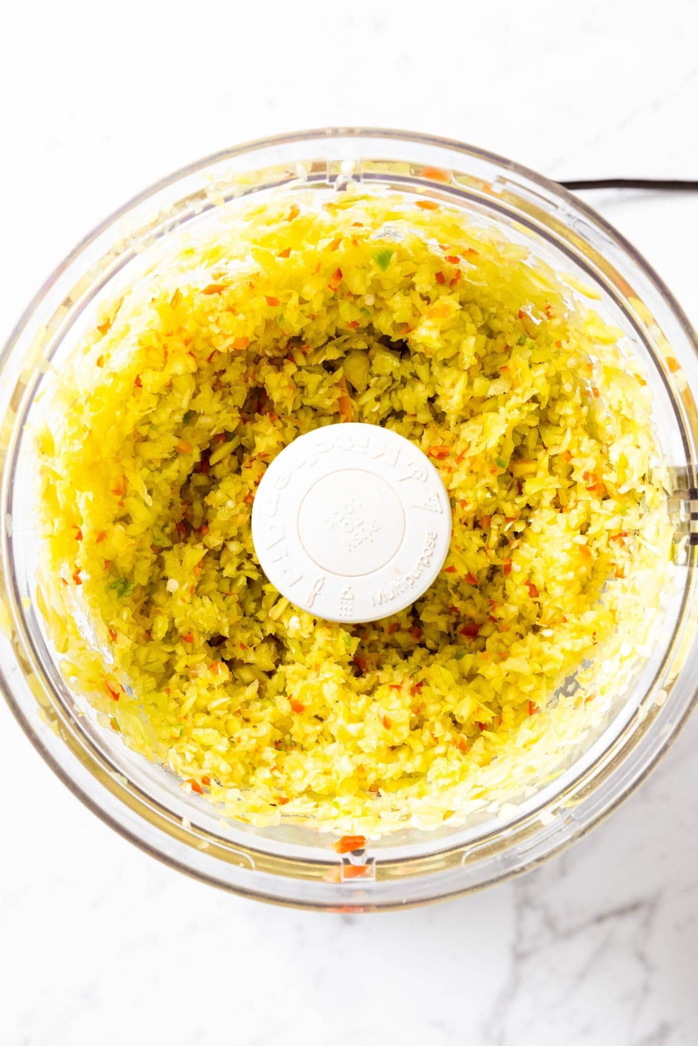 Food processor container filled with chopped up hot peppers in both yellow and red colors.