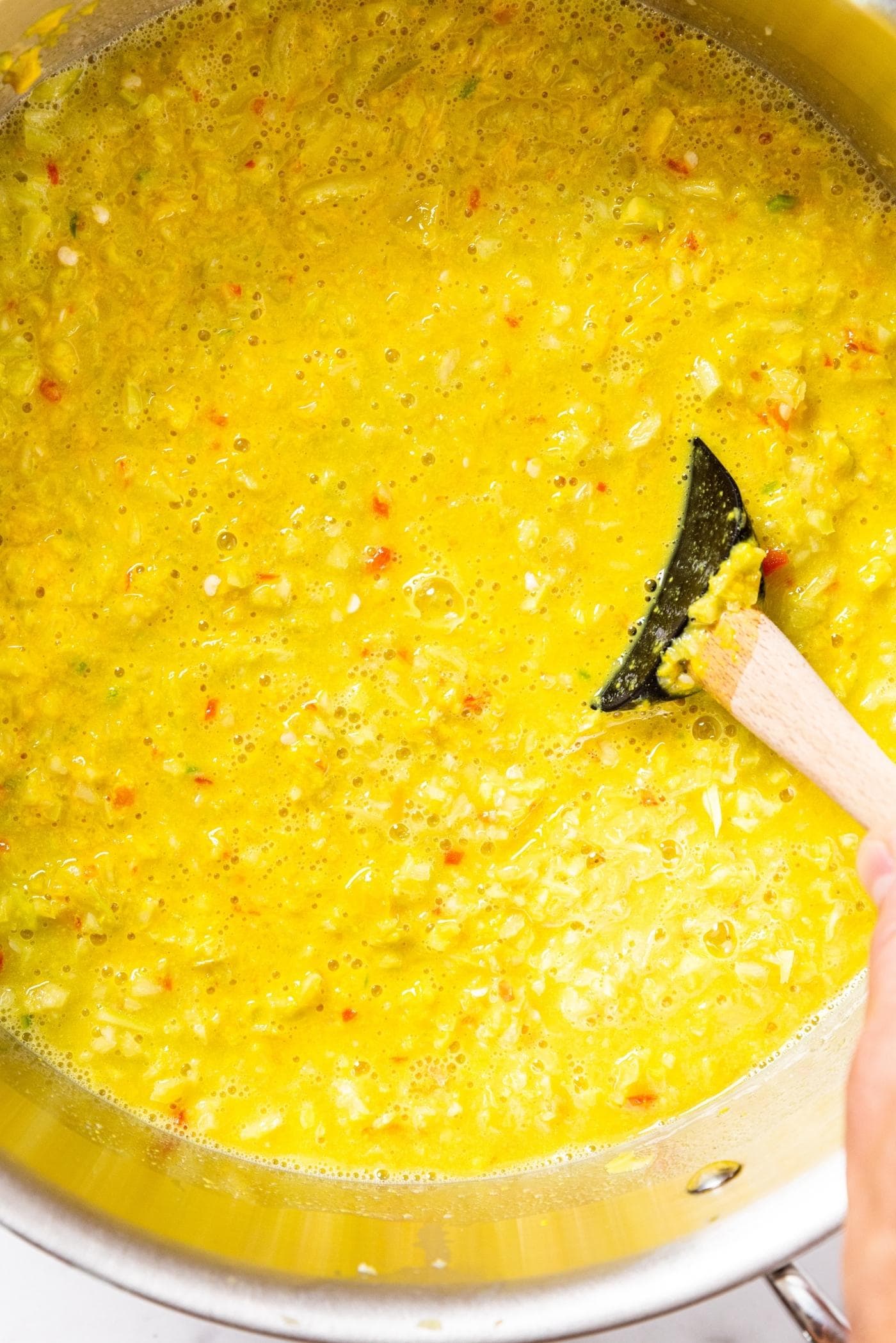 Hand stirring wooden spatula in pepper and mustard mixture in large metal stockpot.