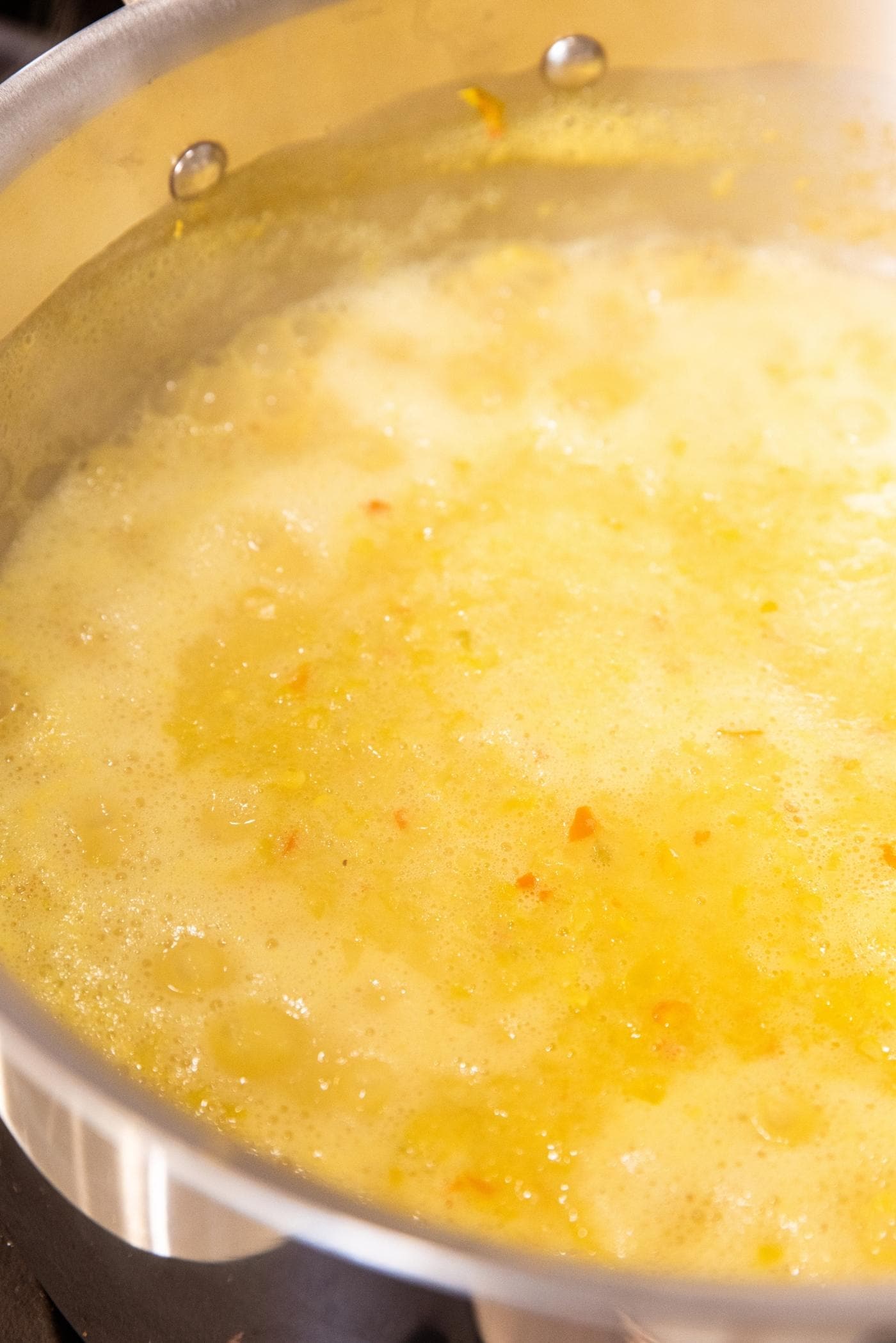 Mustard and pepper mixture in large metal stockpot simmering on stovetop.