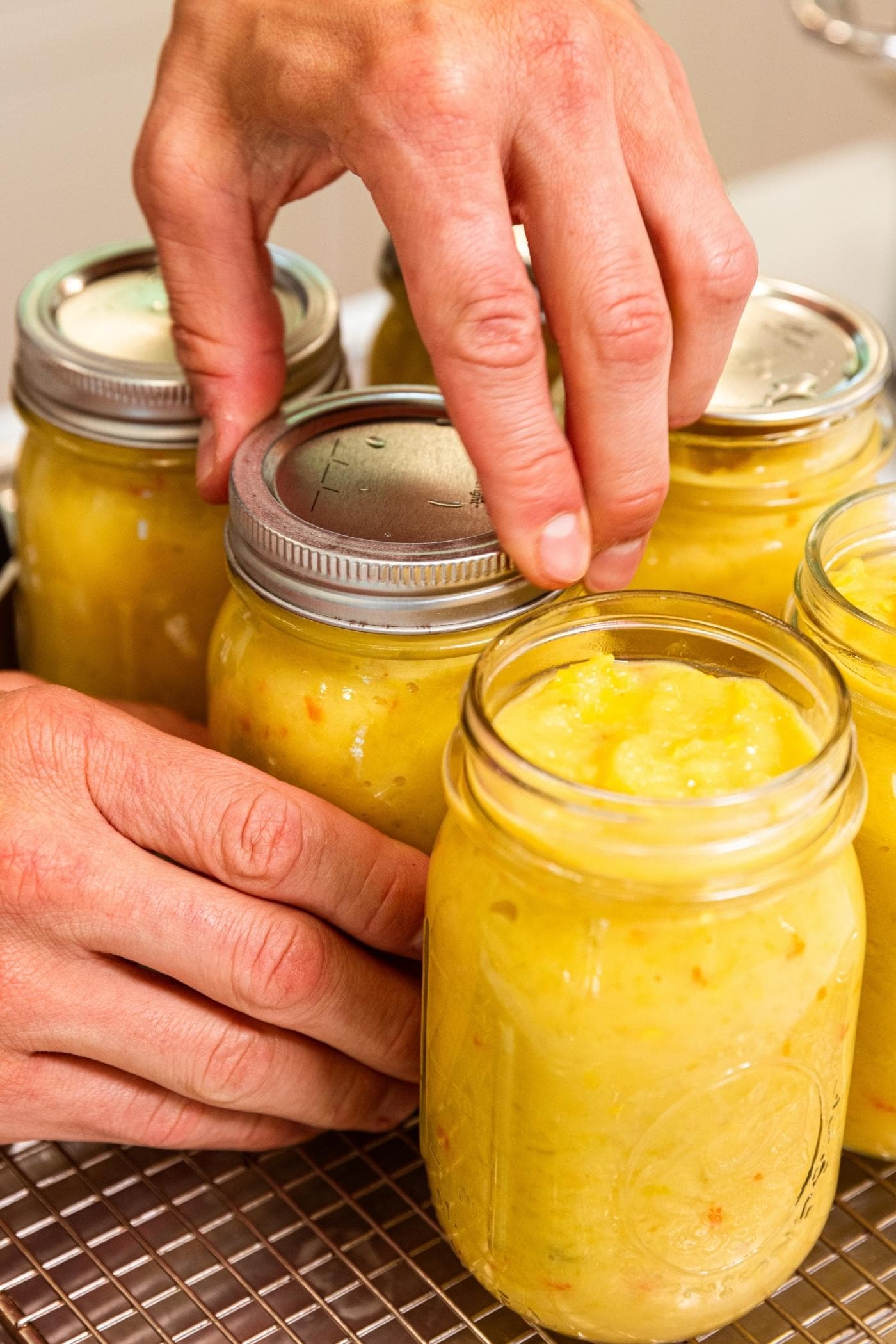Hand putting metal ring on canning jar filled with yellow colored hot pepper mustard.