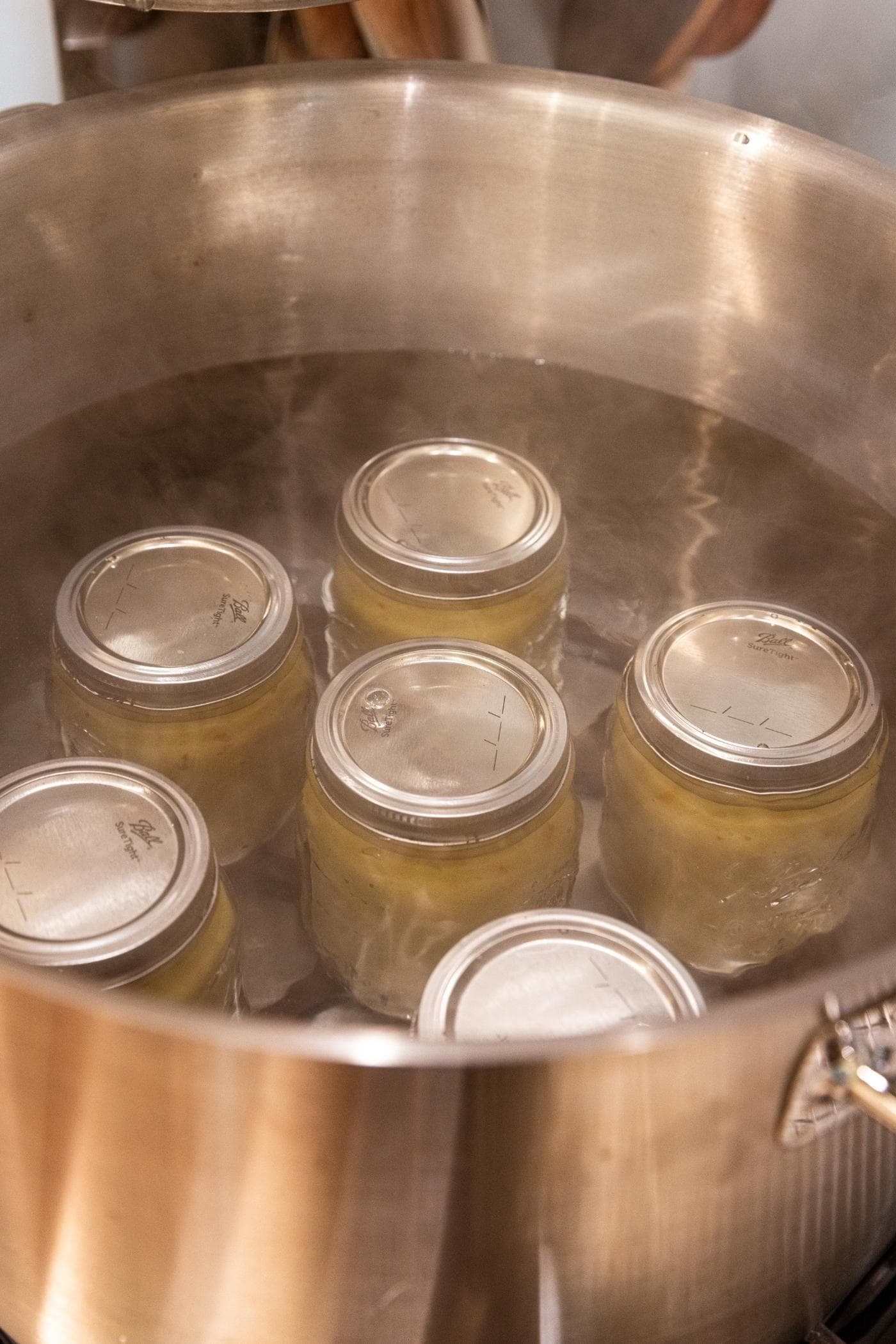 Large metal water bath canner on stove filled with six glass jars filled with hot pepper mustard.