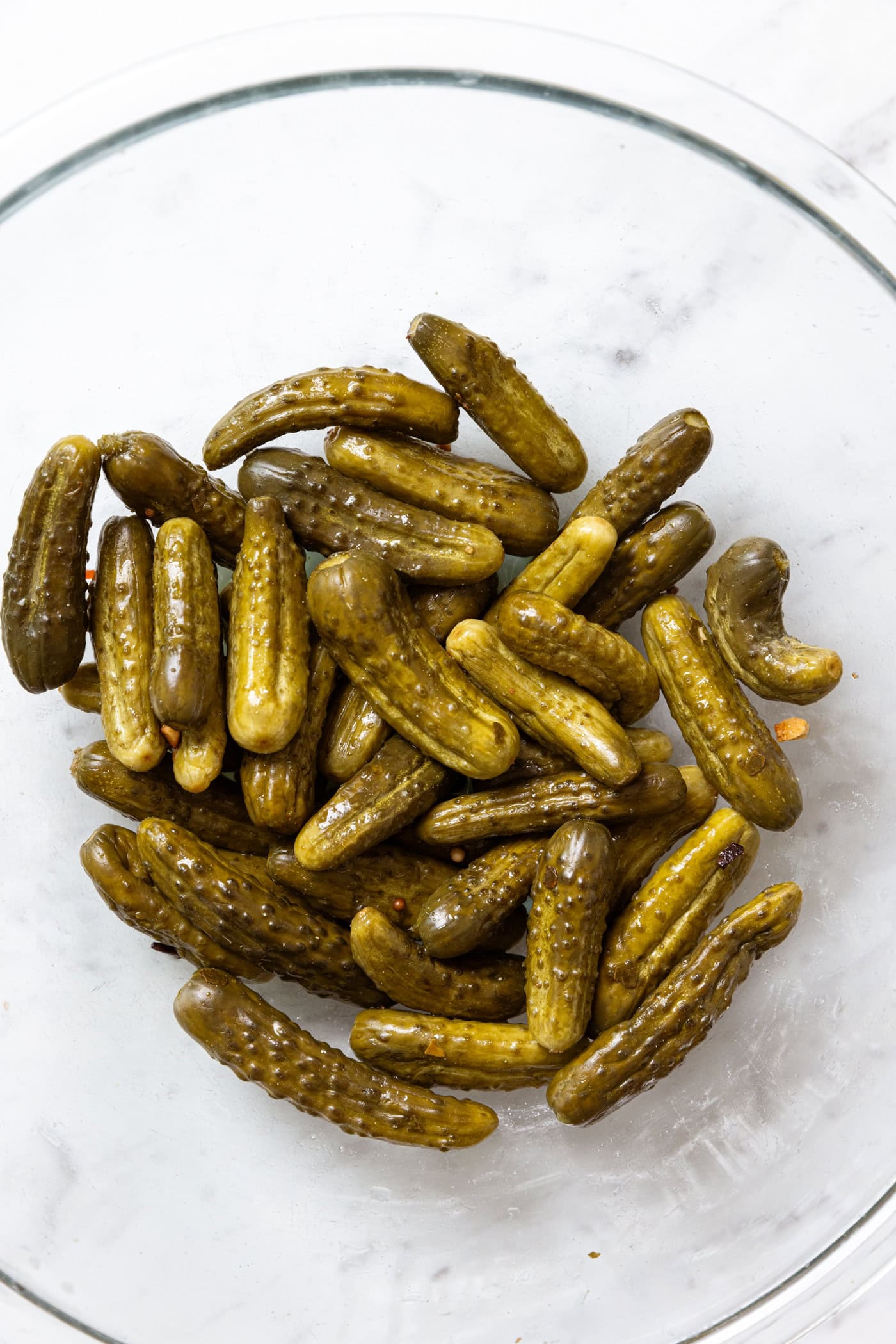 Glass bowl filled with mustard pickles on a marble surface.