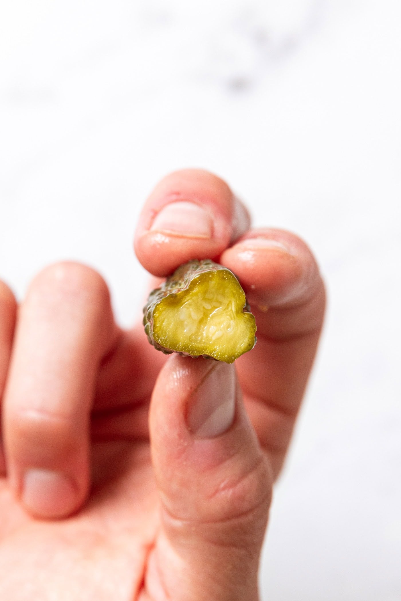 Hand holding a mustard pickle that was bitten in half showing the interior texture of the cucumber.