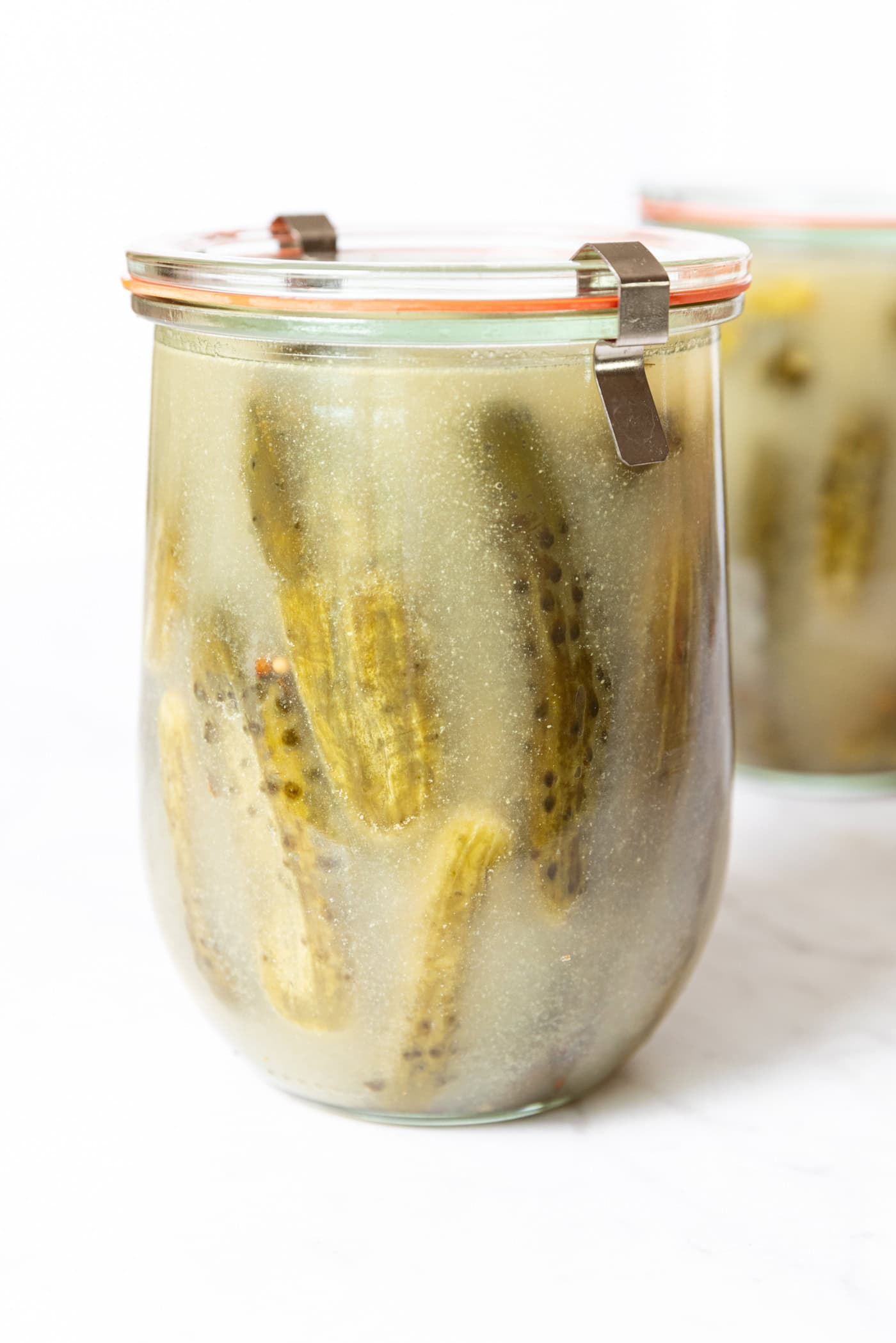 Glass jar filled with brine liquid and pickles in the liquid with lid on top.