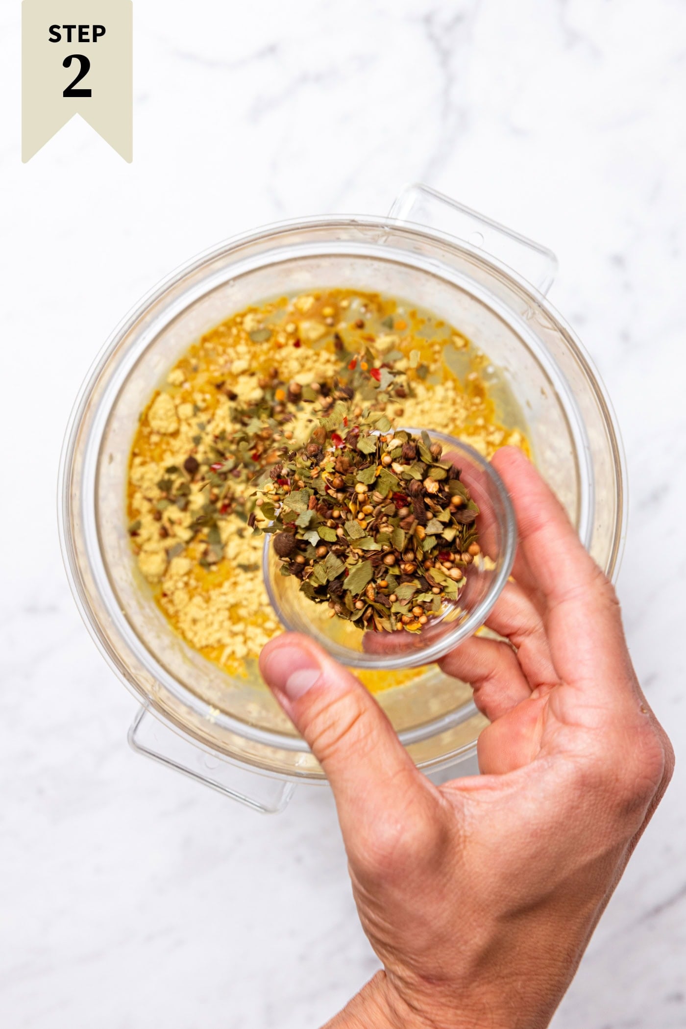 Hand sprinkling pickling spices into a large container filled with vinegar and ground mustard.