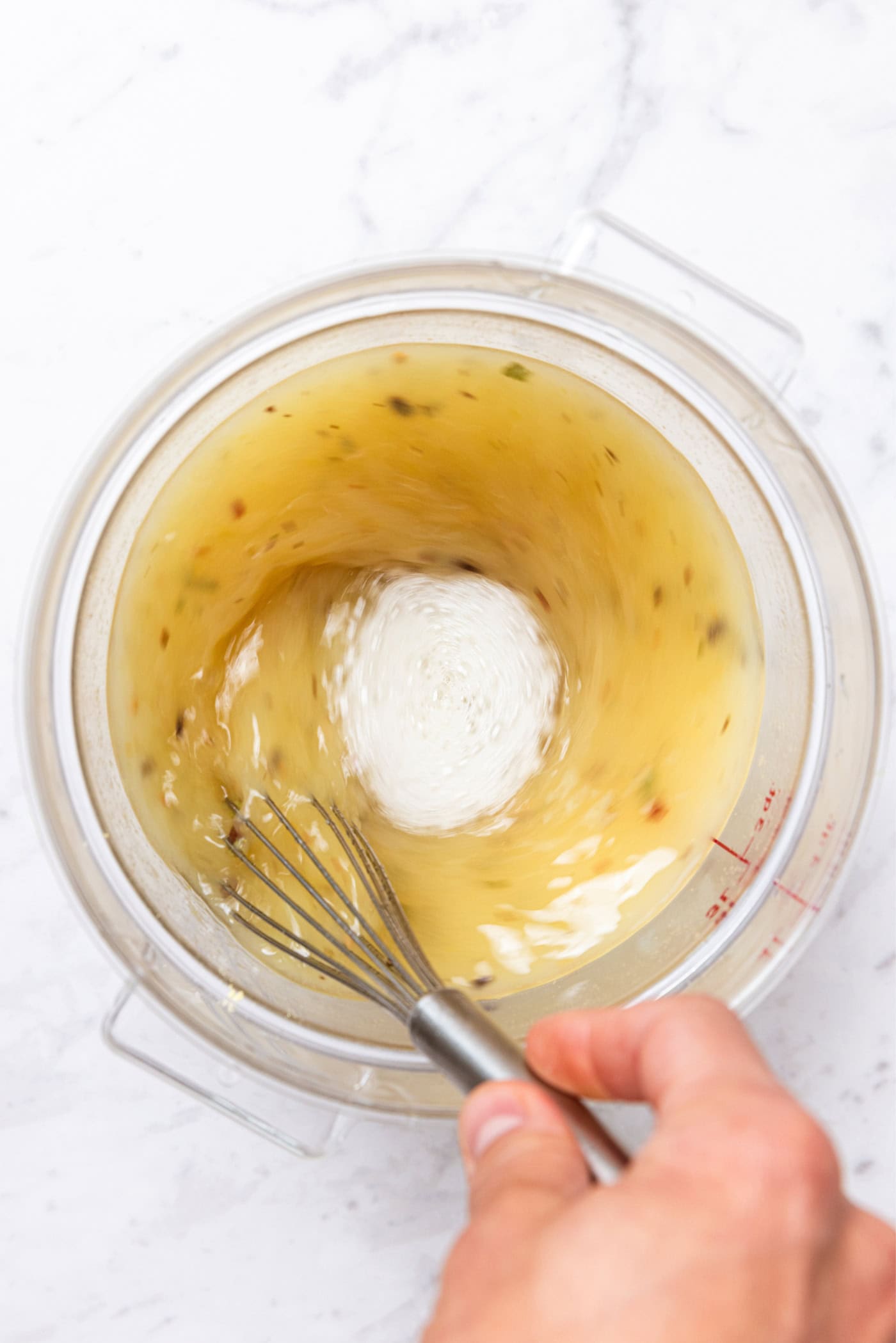 Hand using whisk to mix together brine for mustard pickles recipe.