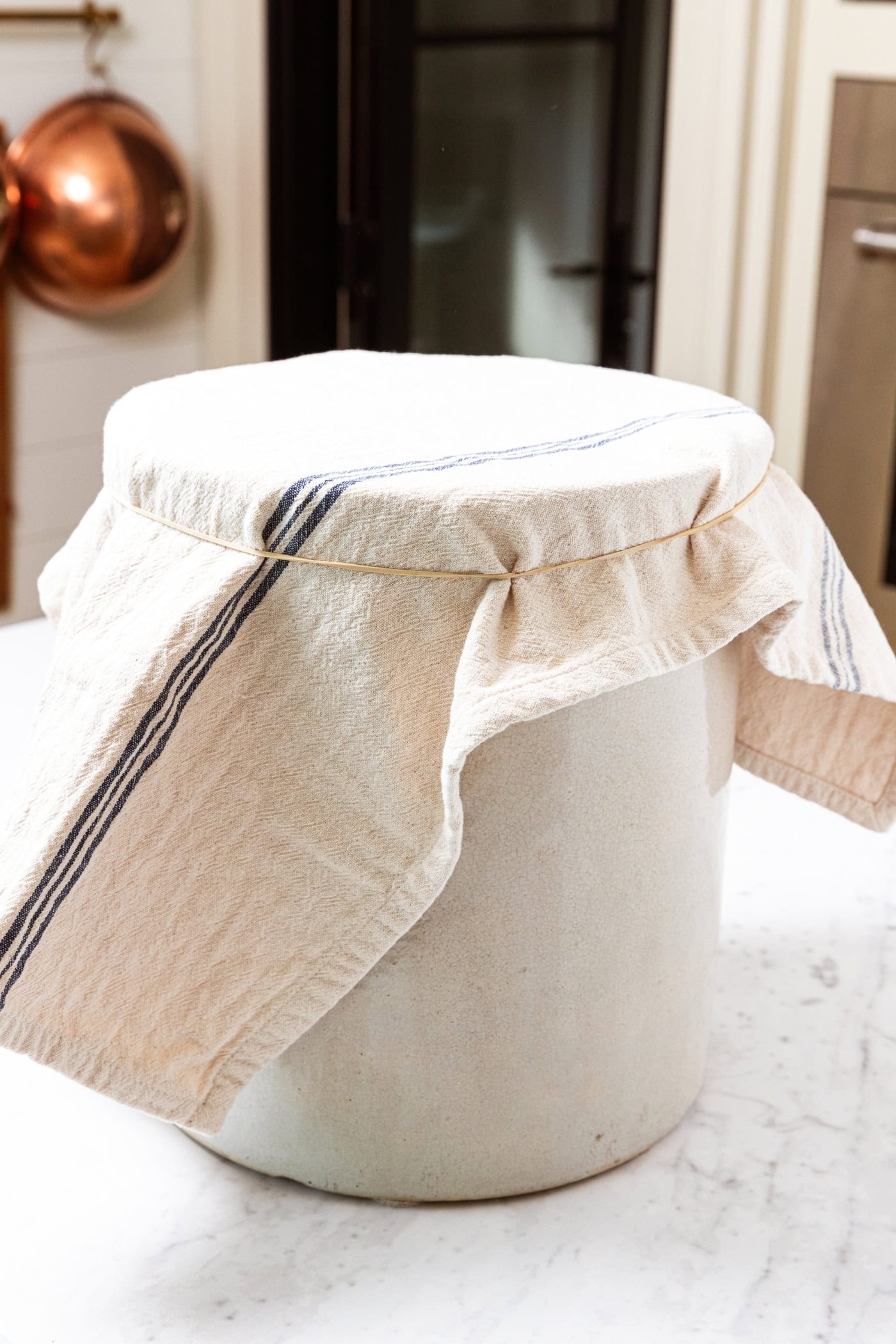 Large crock filled with mustard pickles with cloth secured on top with a rubber band.