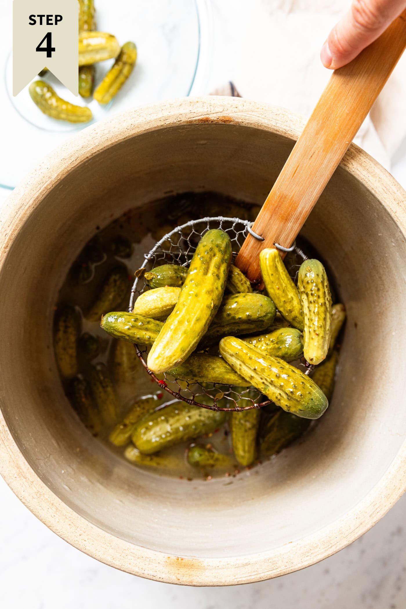 A spider holding mustard pickles above a brine in a large crock.