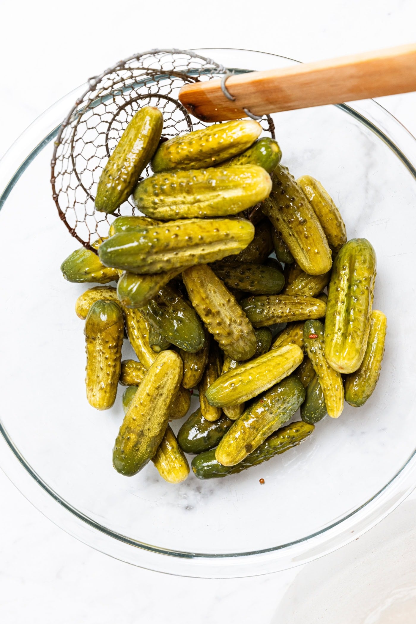 Mustard pickles being removed from a crock into a glass bowl with a spider.
