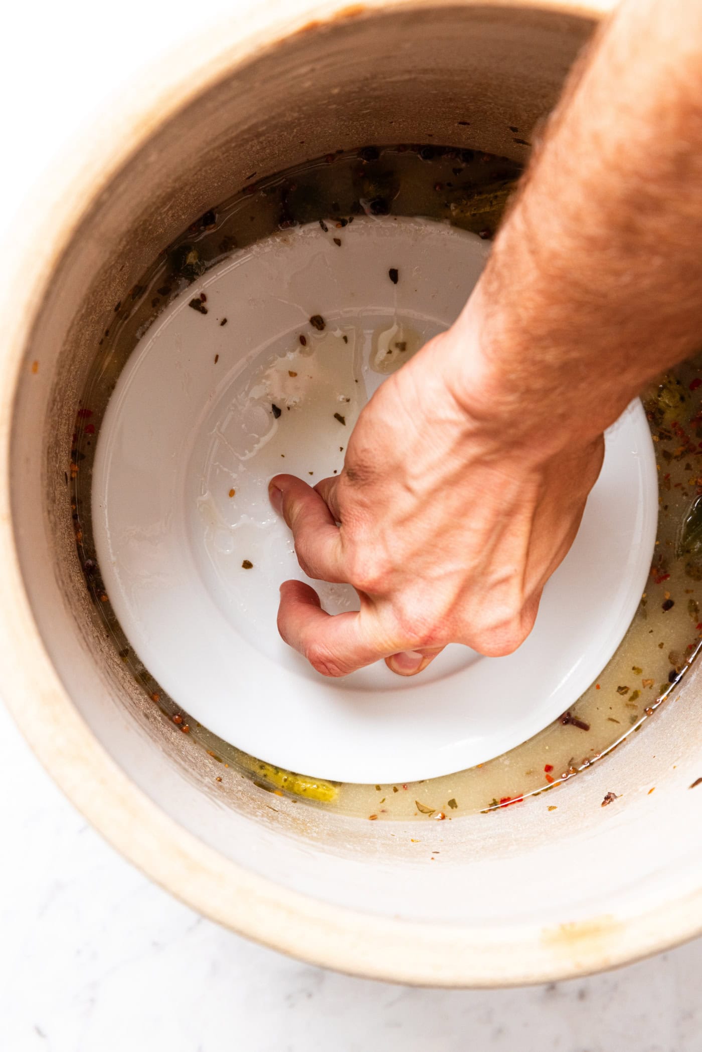 Hand holding plate down on top of brine to keep pickles submerged in a crock.