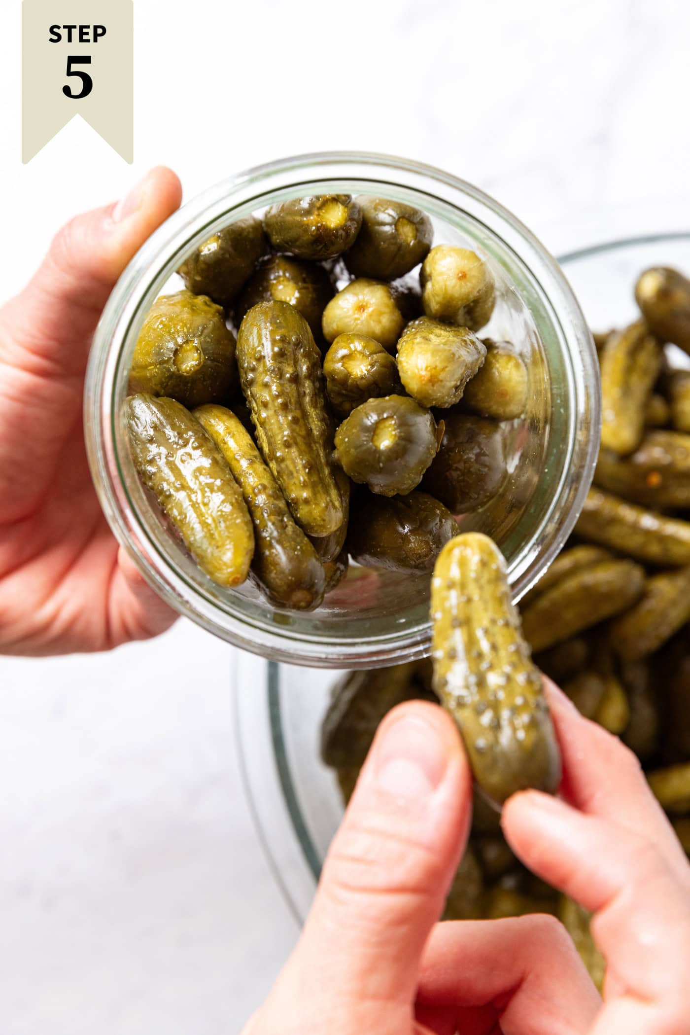 Hand holding glass container fitting mustard pickles into the jar.