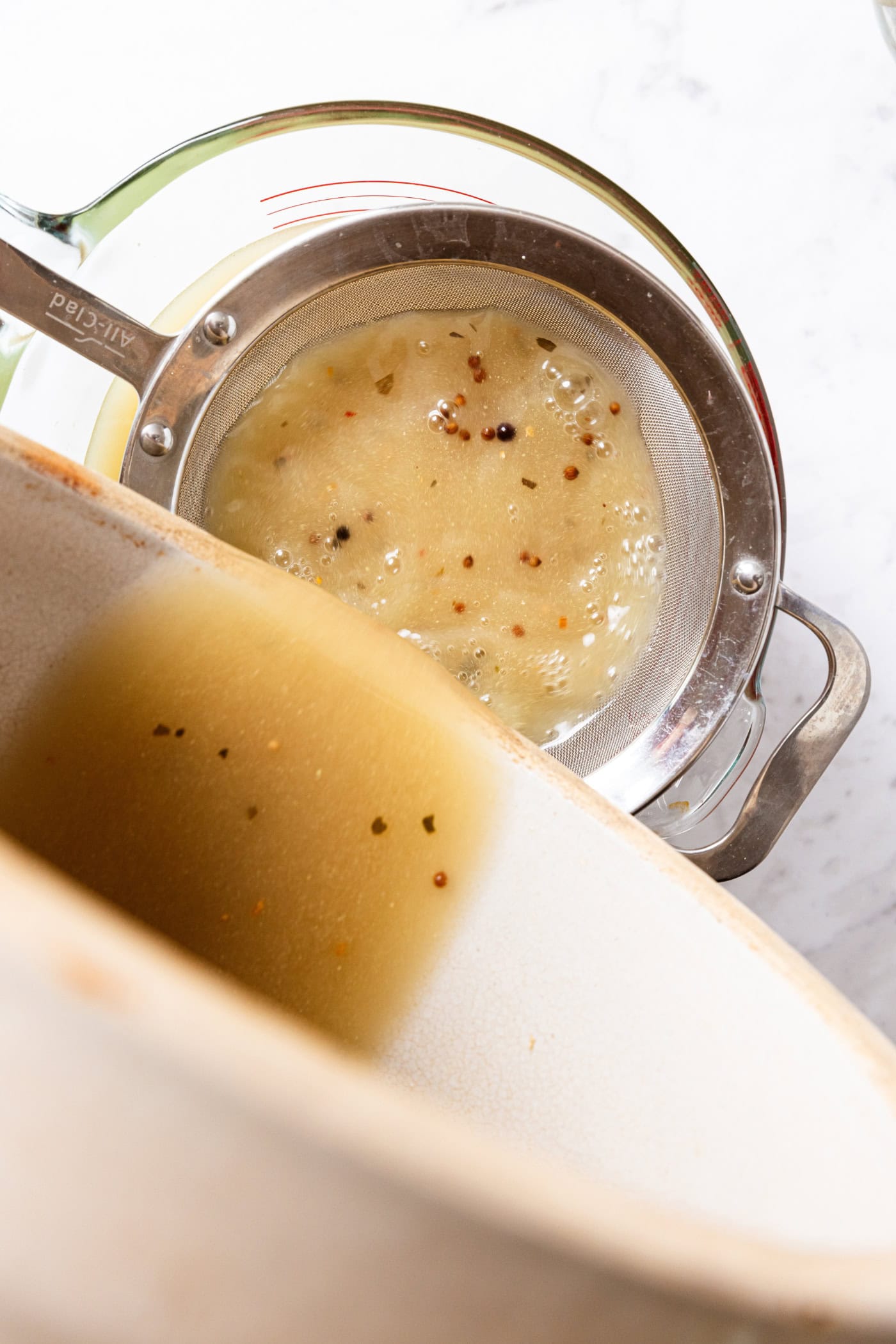 Large crock pouring brining liquid through a colander to get the particles out.