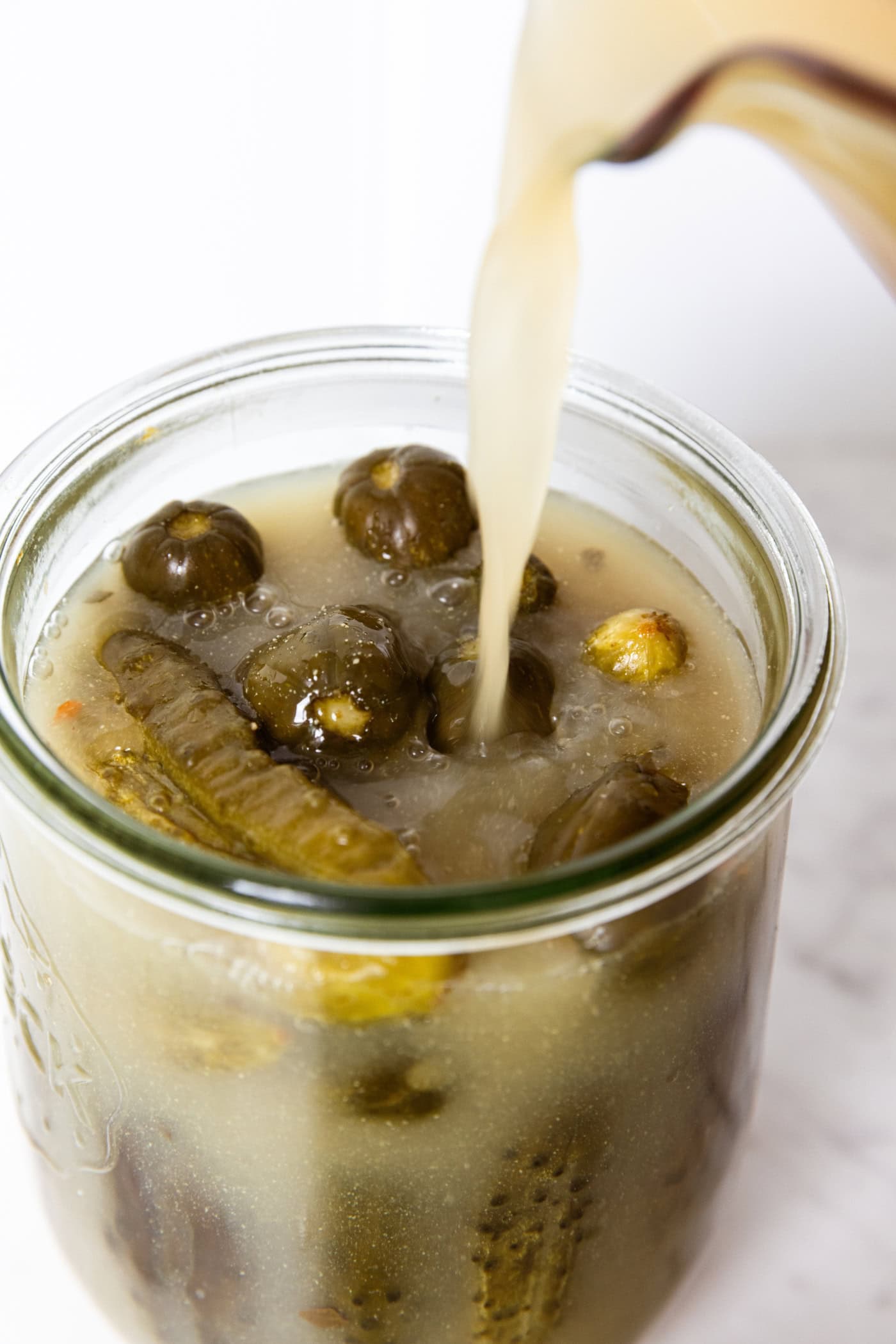 Mustard brine liquid pouring on top of pickles in a glass jar.