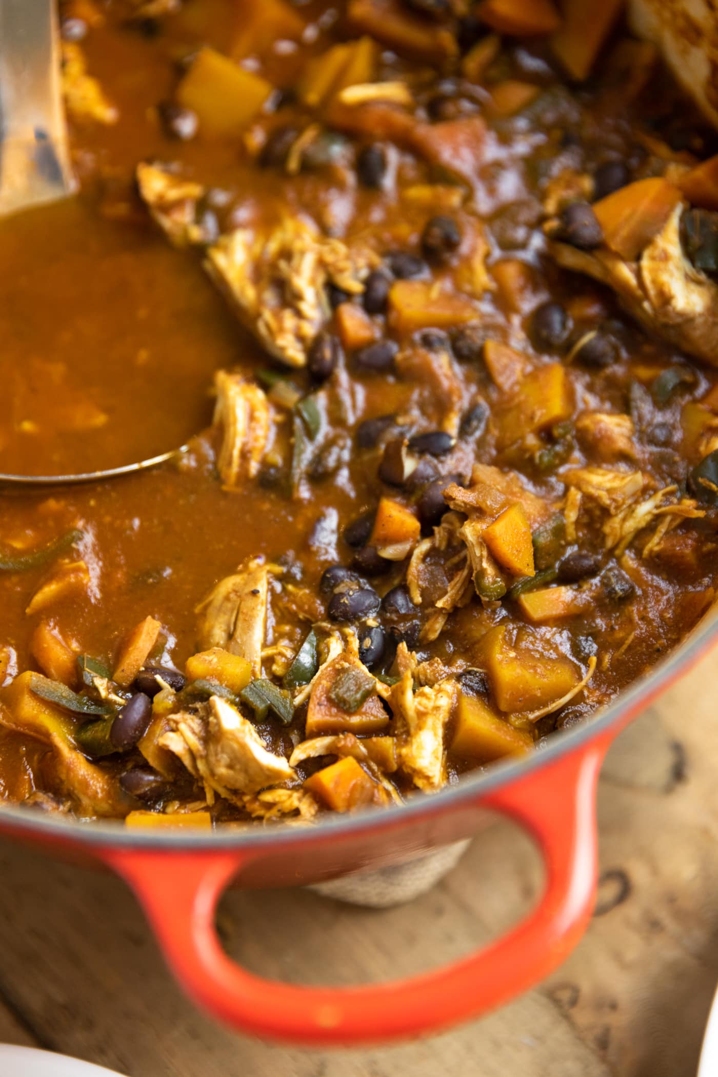Red Dutch oven filled with chili containing black beans and chicken all on wood table