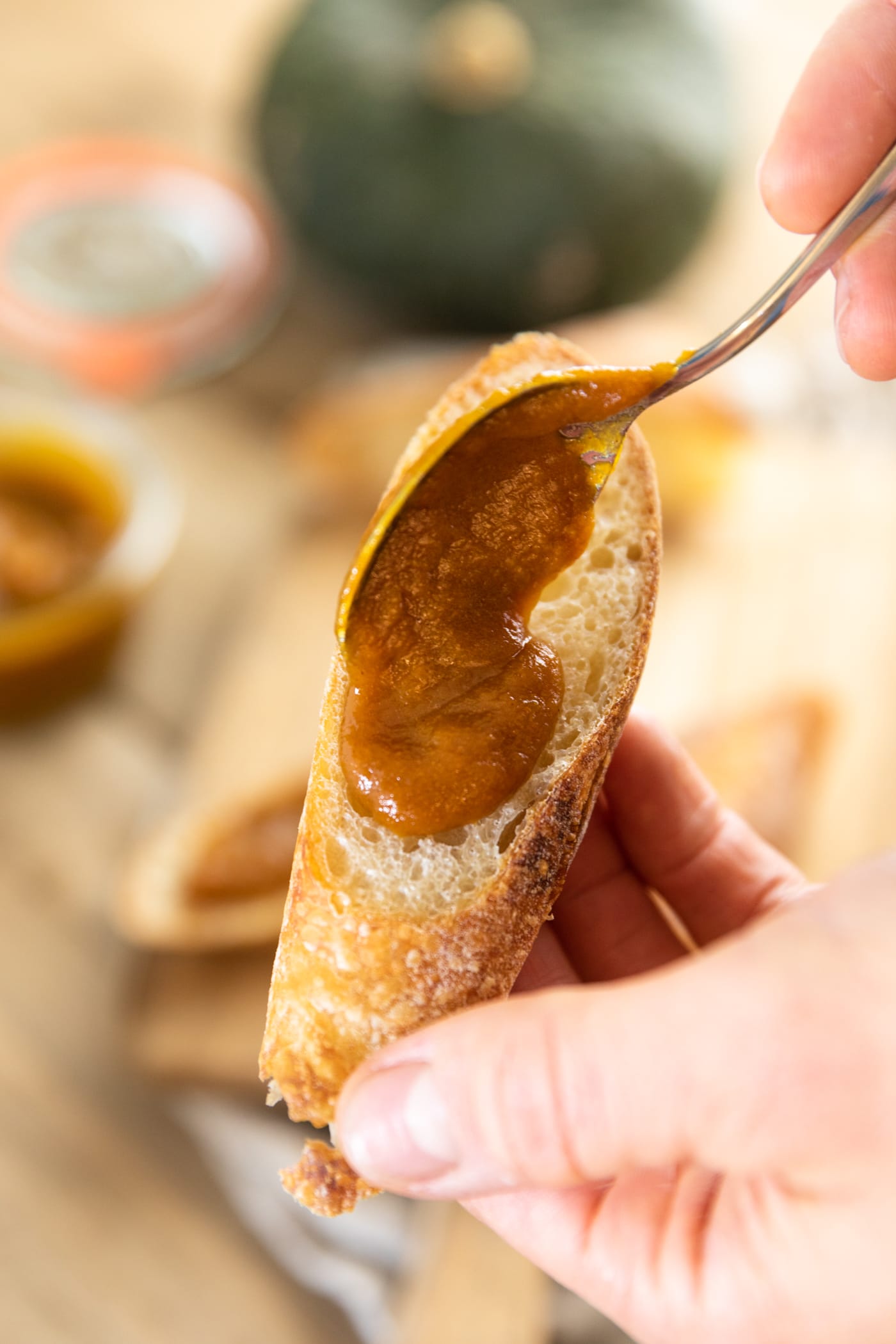 Spoon spreading pumpkin apple butter on top of piece of French bread with extra pieces of bread in background