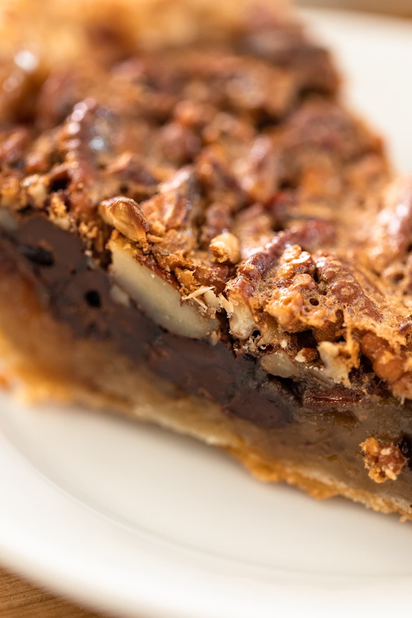 Close up view of side of piece of pecan pie showing chocolate layer along bottom with pie sitting on white plate