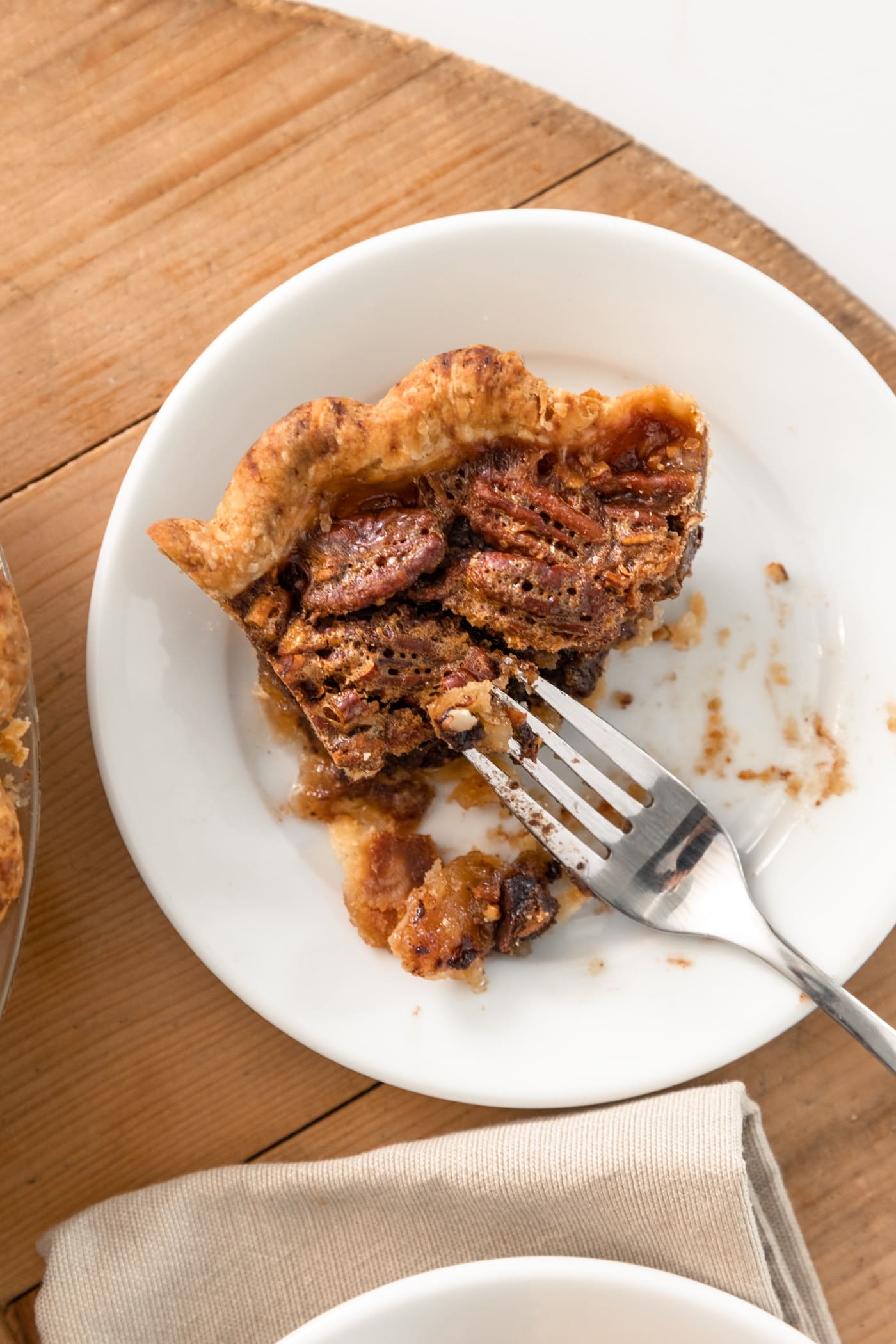 Top down view of half eaten piece of chocolate bourbon pecan pie sitting on white plate with fork sitting on side with napkin all on wooden surface
