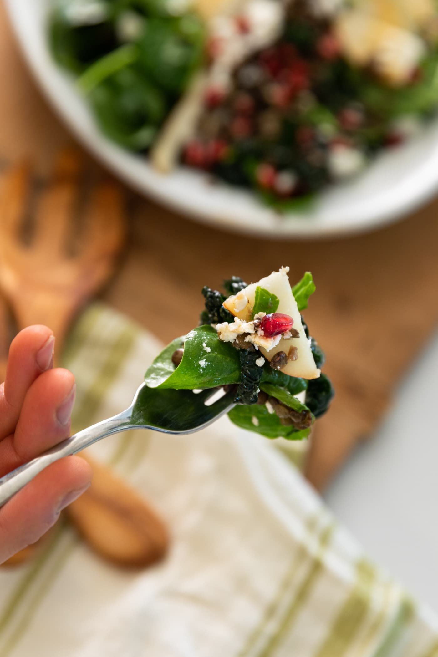 Fork holding bite of salad topped with pomegranate aril and white feta cheese with rest of salad in background