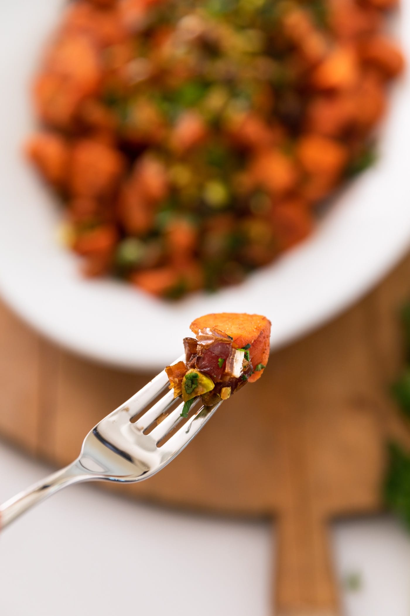 Fork holding carrot and piece of date in front of bowl filled with carrots and wood cutting board