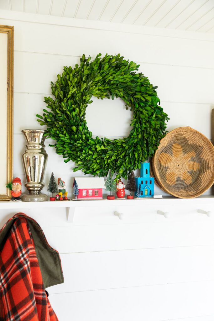 Shelf holding small Christmas ornaments along with green boxwood wreath, bowl, and picture frame