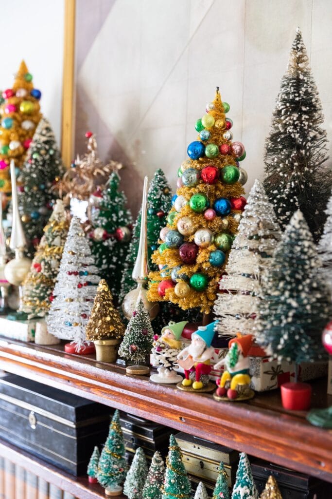 Bottle brush trees of all different shapes and sizes and colors sitting on dark colored wooden shelf