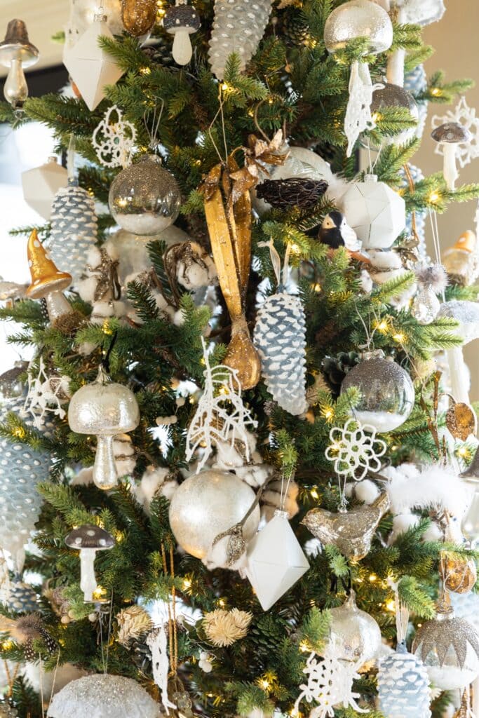 Close up view of gold and silver and white ornaments hanging on tall skinny Christmas tree in front of French doors