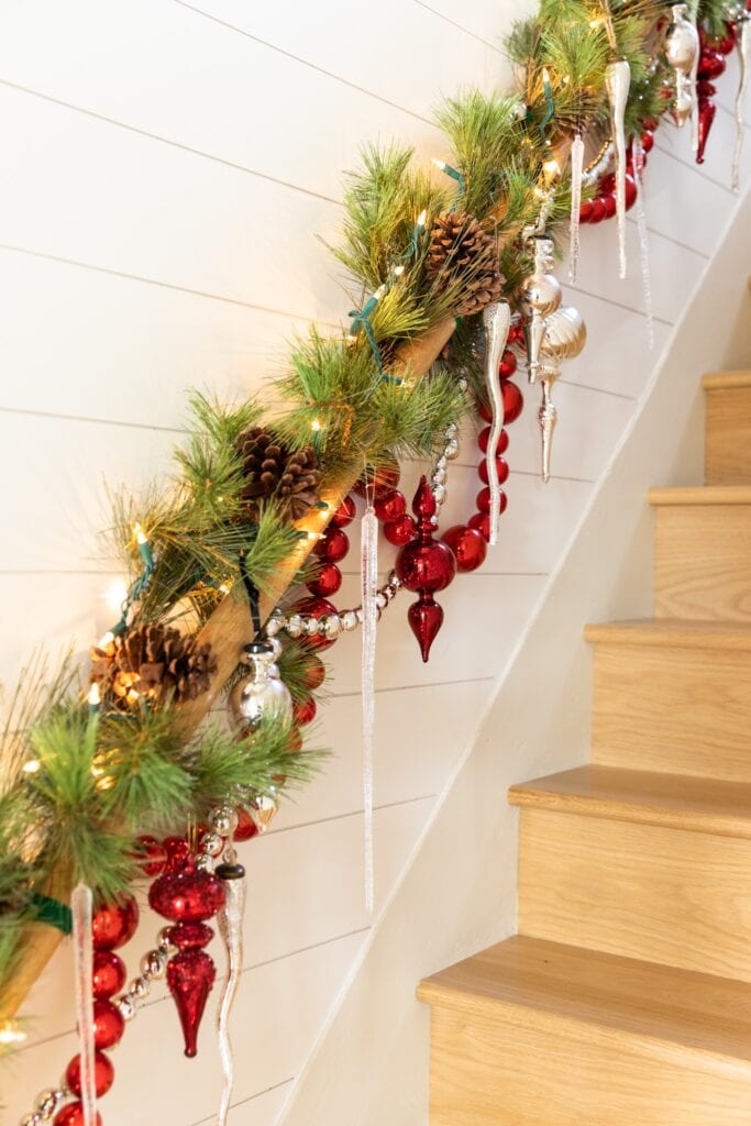 Red and silver ornaments and garland dangling from wood handrail in a stairwell topped with icicles