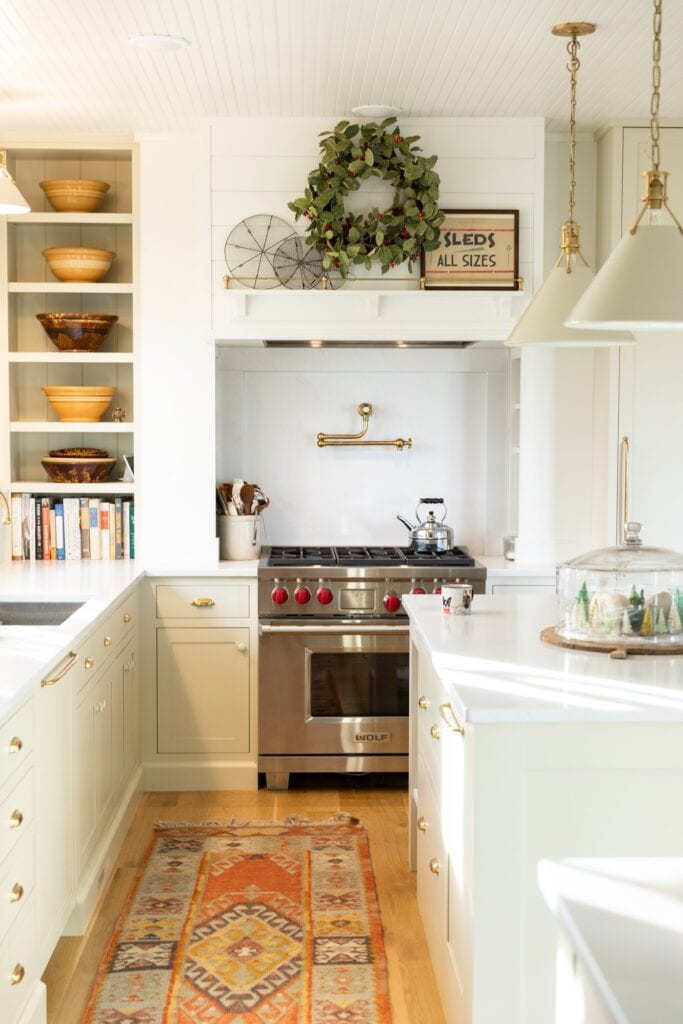 Inside of white kitchen with large range on far side of wall with white countertops and some greenery above the stove