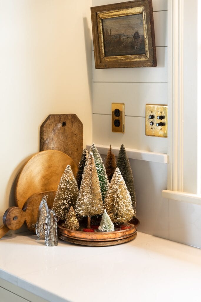 Brown colored bottle brush trees sitting on white countertop with wooden cutting boards behind and small picture hung above